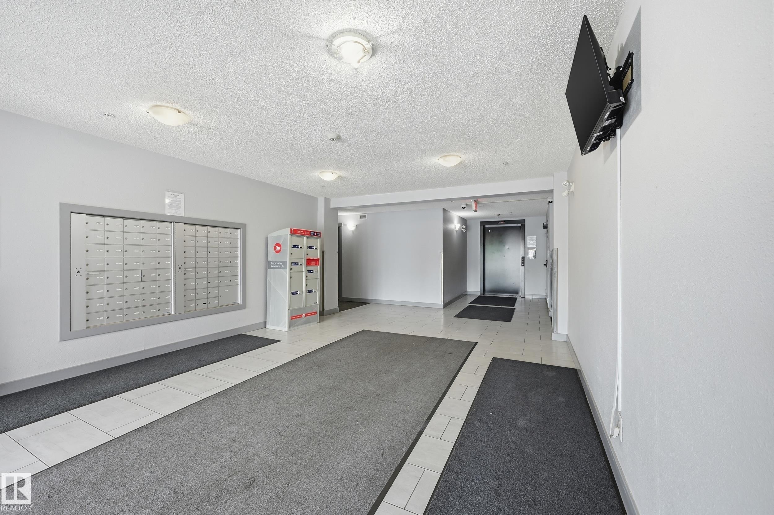 Lobby area featuring built-in mailboxes, secure package lockers, and tile flooring - 304 11804 22 Avenue, Edmonton, AB