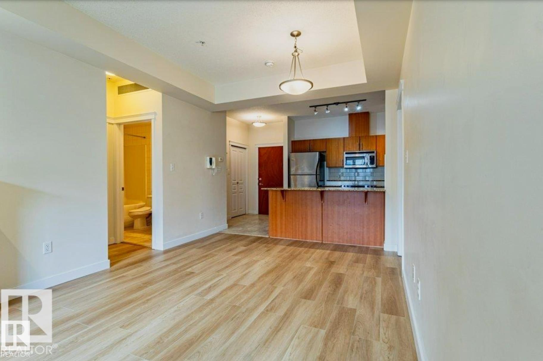 Bright living space featuring wood-finish flooring and a tray ceiling with a hanging fixture - #409 10333 112 St Nw, Edmonton, AB - Indoor Photo Showing Kitchen