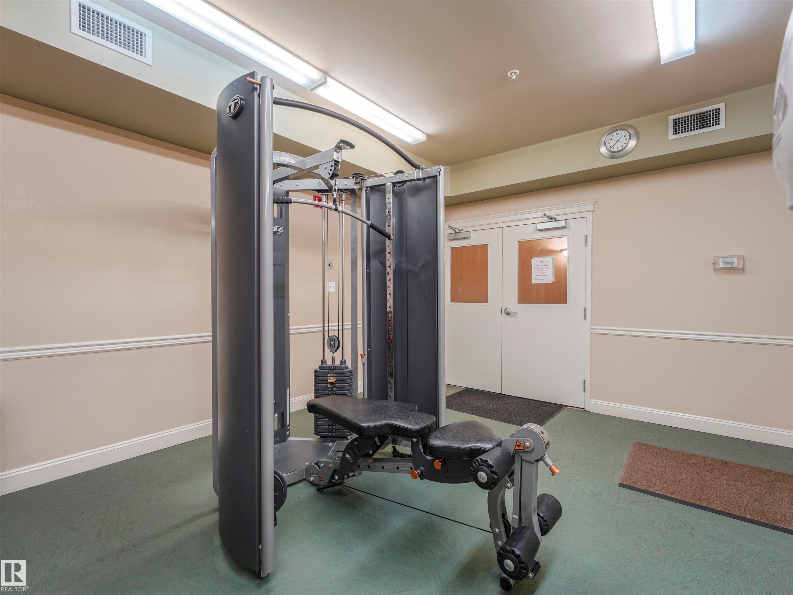 Dedicated fitness area featuring a multi-station exercise machine, neutral wall tones with chair rail molding, and a textured green floor - #409 10333 112 St Nw, Edmonton, AB - Indoor