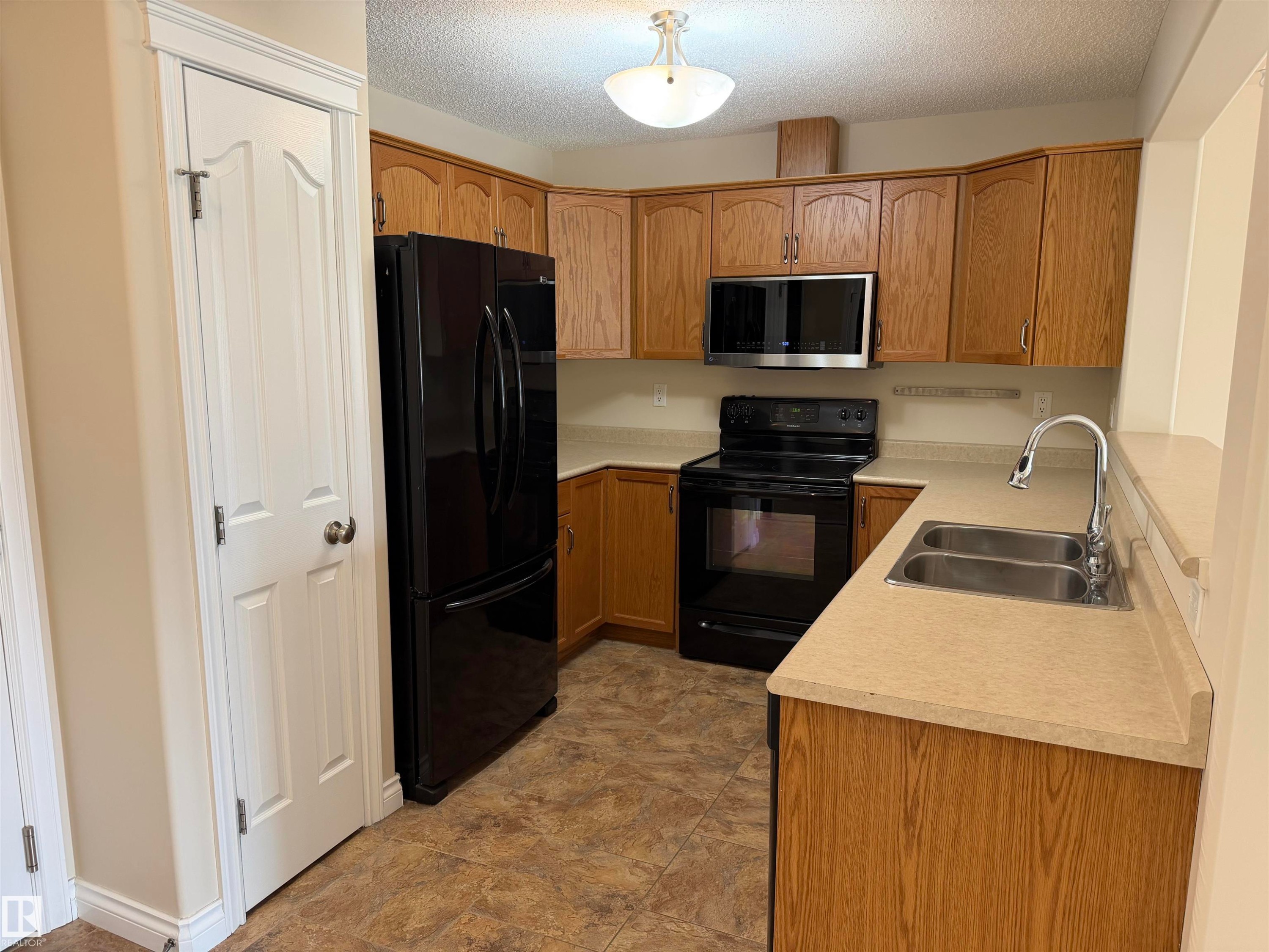 Kitchen featuring wood-finish cabinetry, laminate countertops, and stainless steel double sink - 118 7801 Golf Course Road, Stony Plain, AB