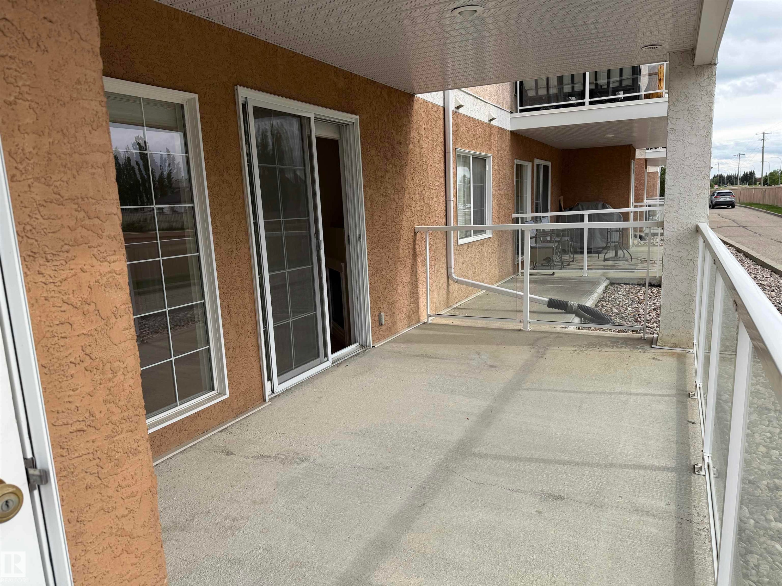 Concrete patio featuring a glass and aluminum railing system, stucco exterior, and sliding glass door access - 118 7801 Golf Course Road, Stony Plain, AB