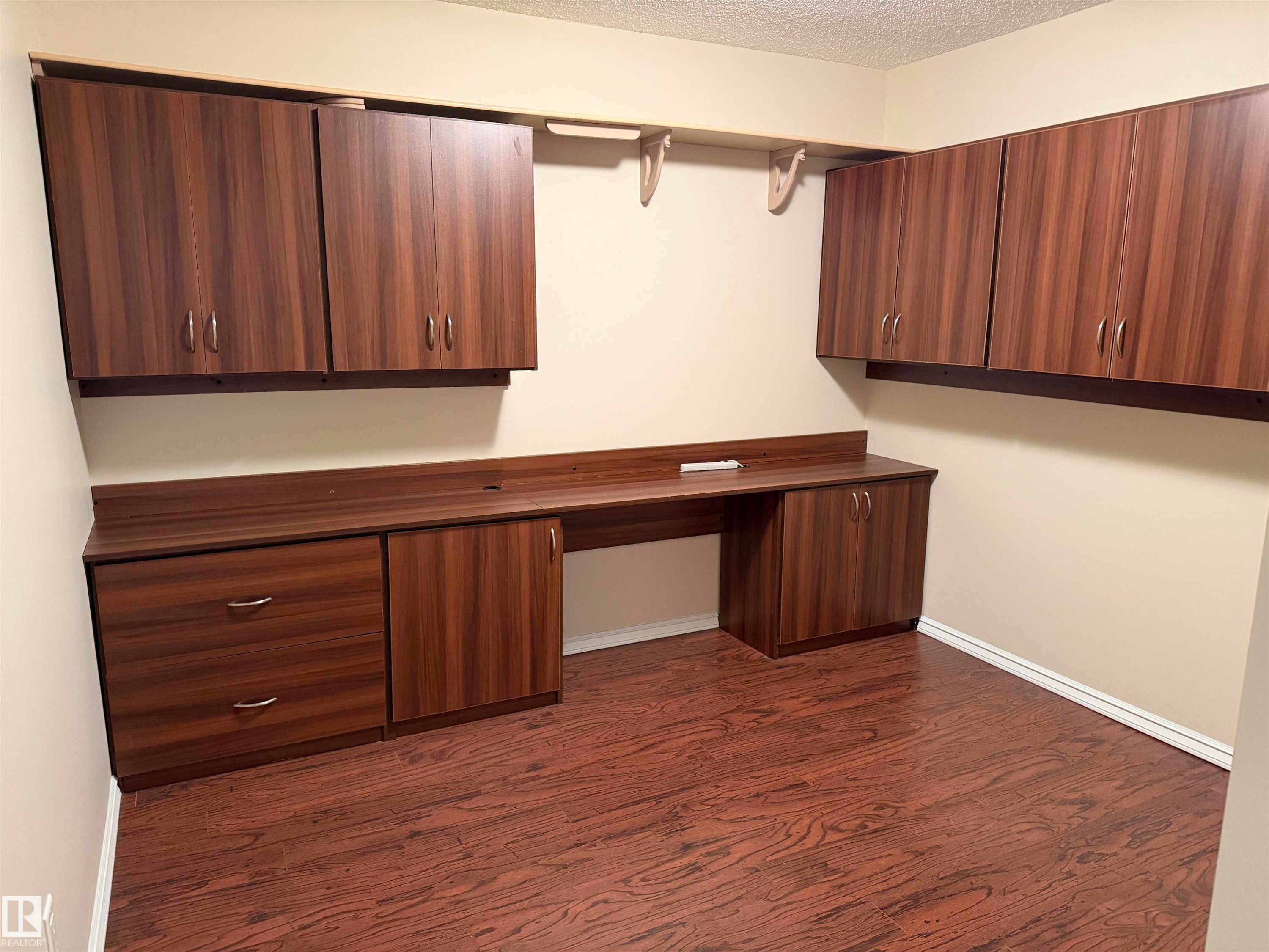 Built-in wood-finish cabinetry and desk surface with integrated power outlets, complemented by wood-finish flooring - 118 7801 Golf Course Road, Stony Plain, AB