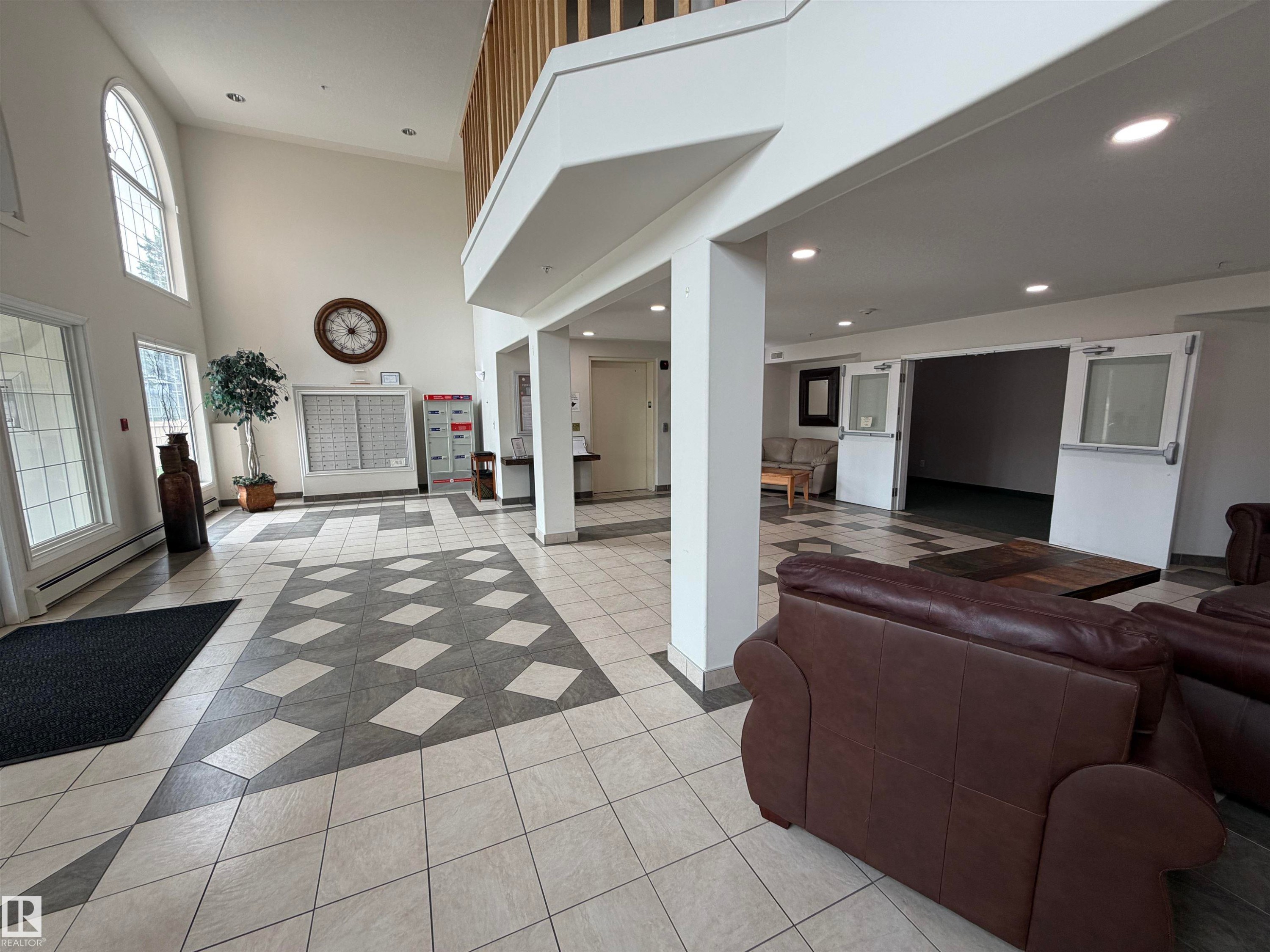 Spacious common area featuring an arched window, high ceilings, patterned tile flooring, and a second-story balcony overlook - 118 7801 Golf Course Road, Stony Plain, AB