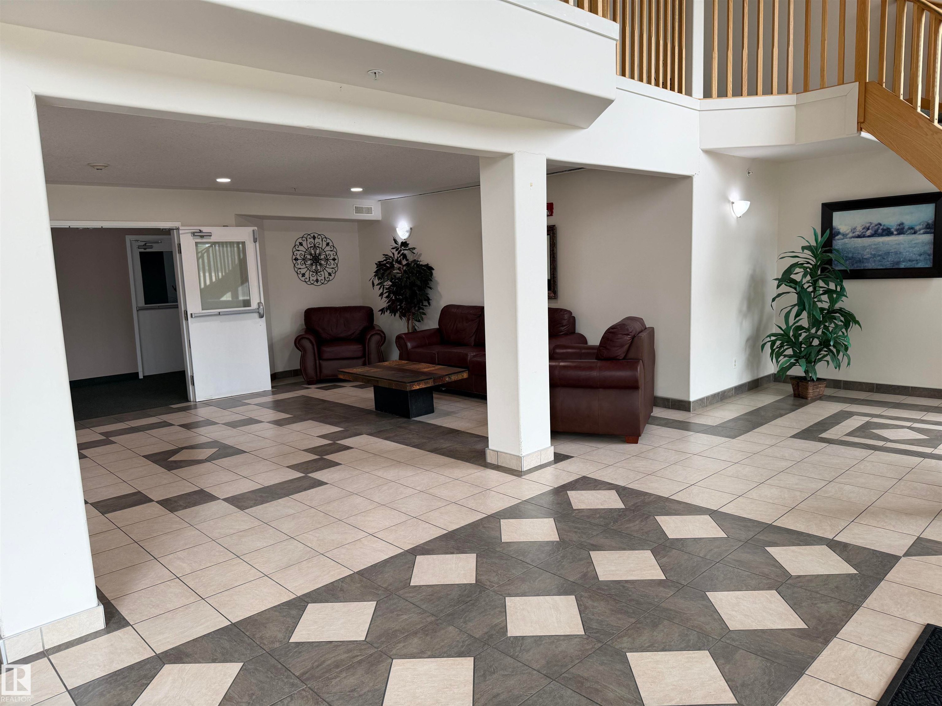 Two-story foyer featuring patterned tile flooring, a prominent wooden staircase with open railings, and recessed ceiling lighting - 118 7801 Golf Course Road, Stony Plain, AB