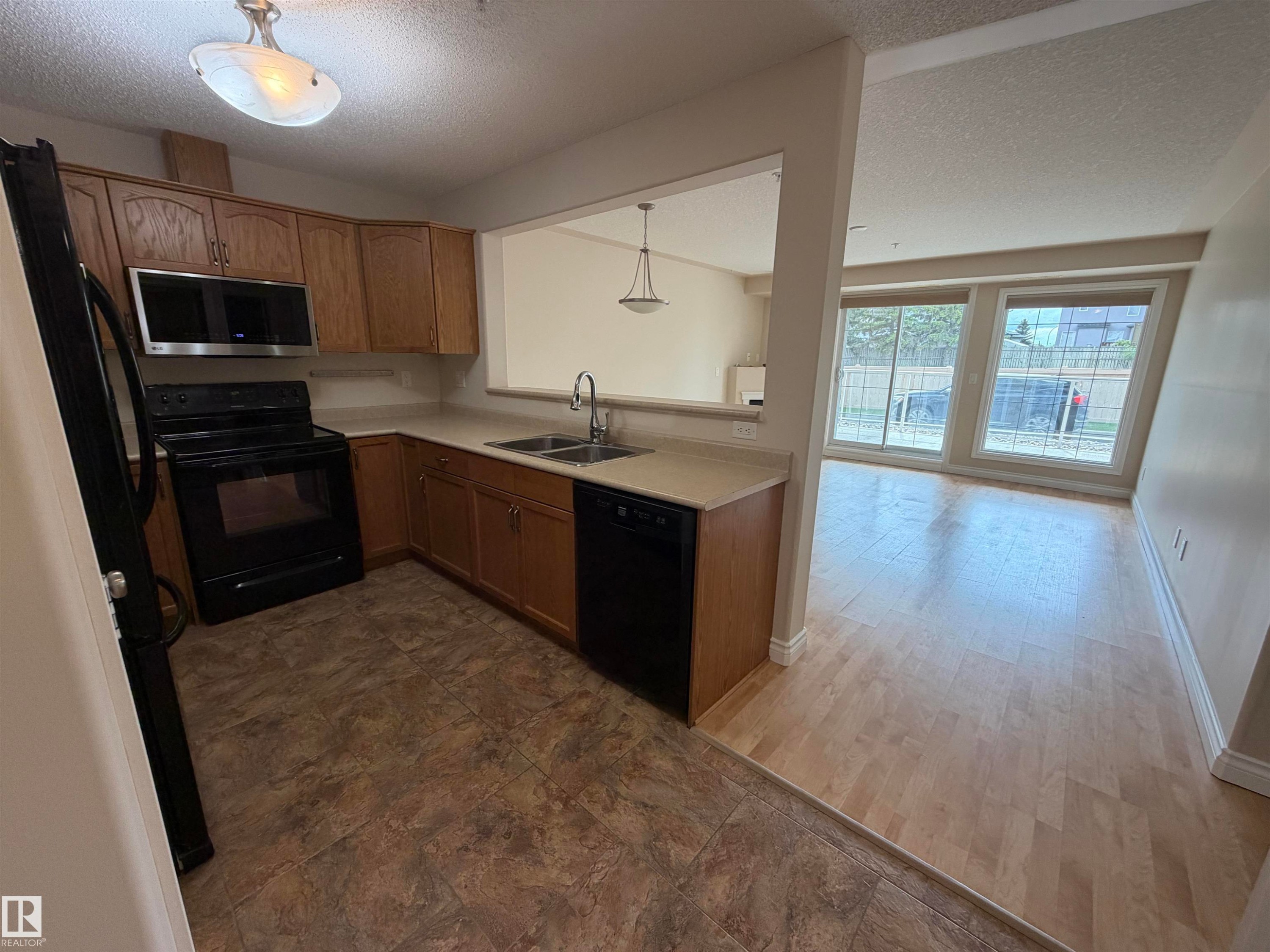 Kitchen featuring wood cabinetry, black appliances including a built-in microwave, and light-toned countertops - 118 7801 Golf Course Road, Stony Plain, AB