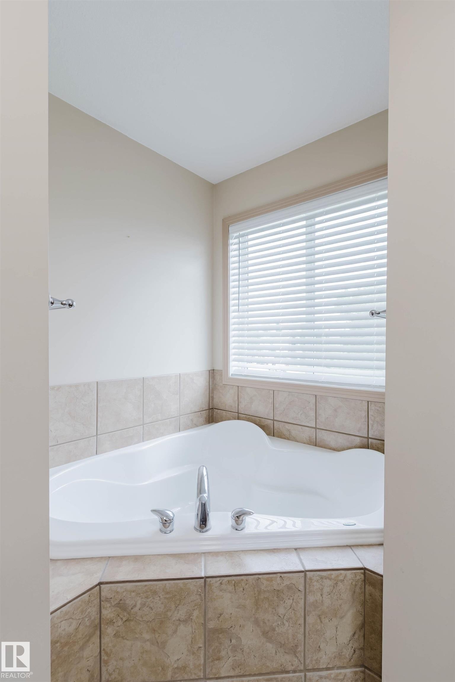 Corner soaking tub with chrome fixtures, surrounded by neutral-toned tile - 2236 Garnett Crest, Edmonton, AB