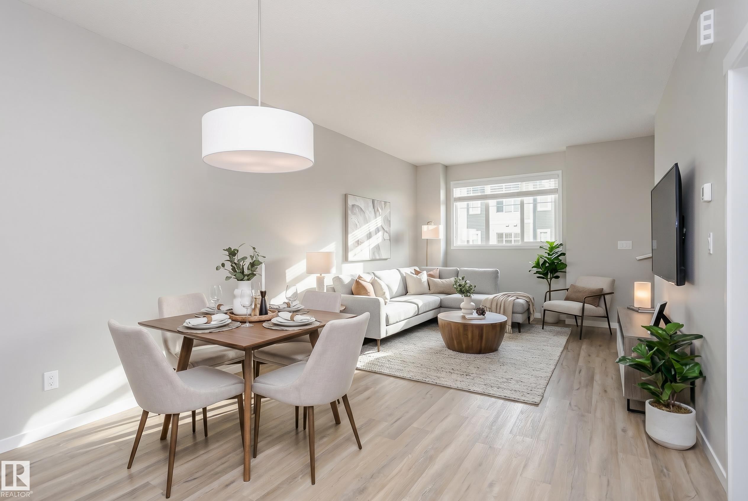 Open-concept living space featuring light wood-finish flooring, a contemporary drum pendant light, a large window, and neutral-toned walls - 320 Secord Boulevard, Edmonton, AB - Indoor