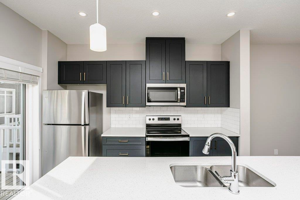 The kitchen features stainless steel appliances, dark cabinetry, and white countertops - 320 Secord Boulevard, Edmonton, AB - Indoor Photo Showing Kitchen With Stainless Steel Kitchen With Upgraded Kitchen
