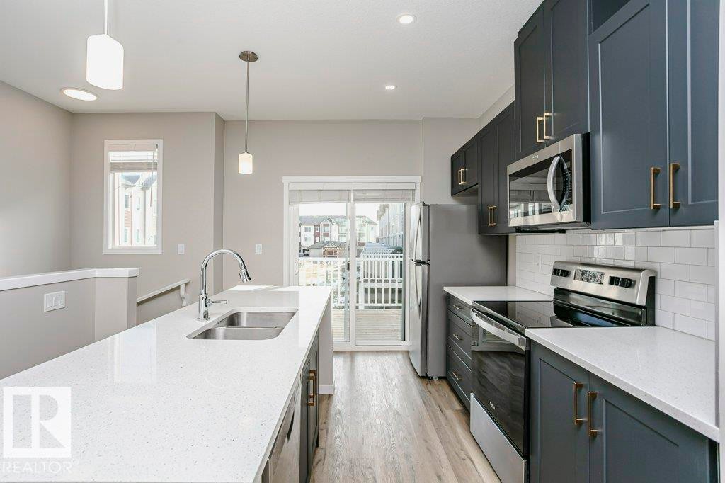 The kitchen features a spacious island with a sink, white countertops, and dark cabinetry with gold-toned hardware - 320 Secord Boulevard, Edmonton, AB - Indoor Photo Showing Kitchen With Stainless Steel Kitchen With Double Sink With Upgraded Kitchen