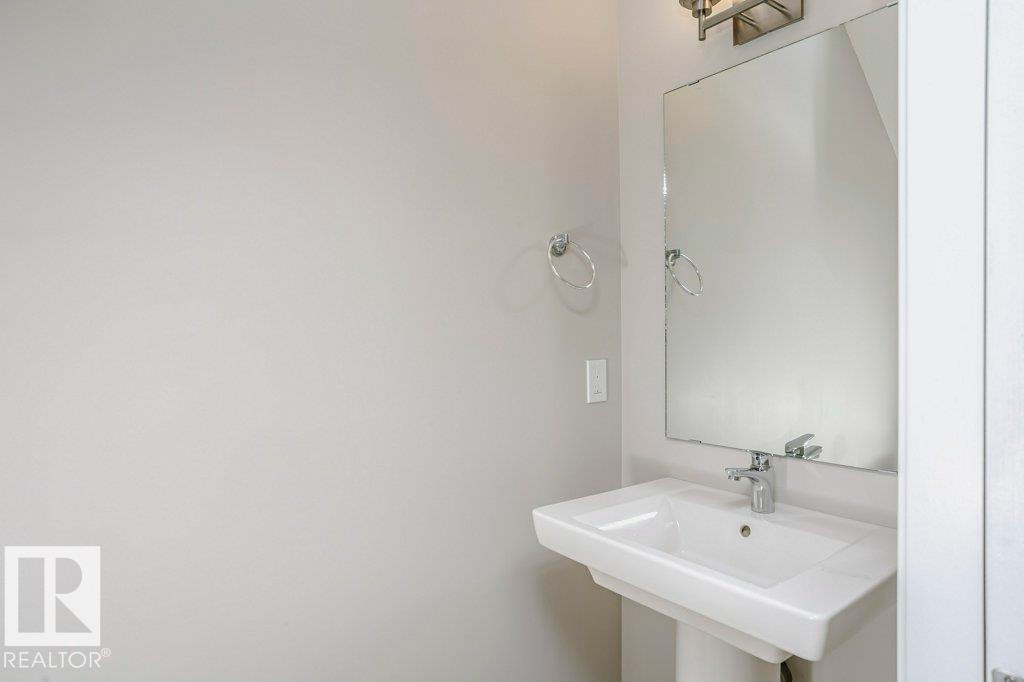 Bathroom featuring a pedestal sink with a chrome faucet, a rectangular mirror, and a wall-mounted light fixture - 320 Secord Boulevard, Edmonton, AB - Indoor Photo Showing Bathroom