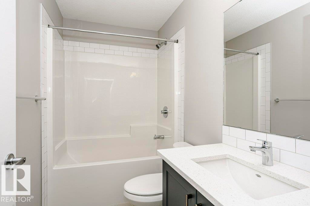 Bathroom featuring a white subway tile backsplash, a vanity with a white countertop and an integrated sink, and a white bathtub with a shower - 320 Secord Boulevard, Edmonton, AB - Indoor Photo Showing Bathroom