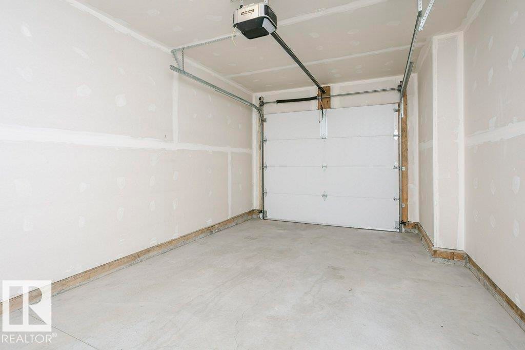 The property includes a garage with a concrete floor, an automatic garage door opener, and unfinished drywall walls - 320 Secord Boulevard, Edmonton, AB - Indoor Photo Showing Garage