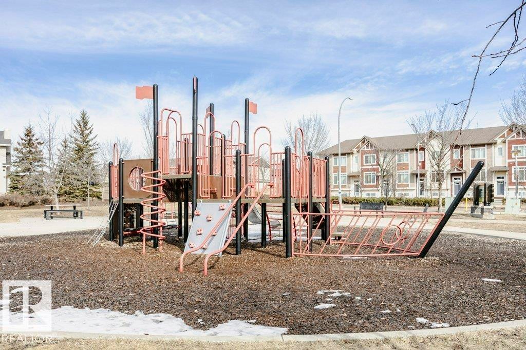 This community features a playground with a ship-themed structure, set on a dark ground covering, and surrounded by bare trees - 320 Secord Boulevard, Edmonton, AB - Outdoor