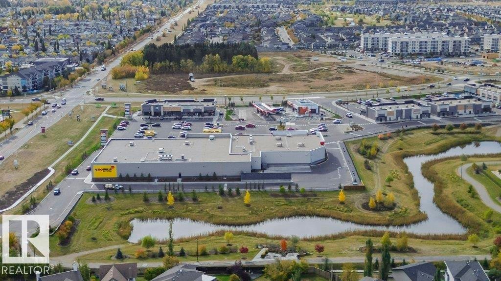 Aerial view showcasing the property's surrounding commercial buildings, a paved road with vehicles, and green spaces featuring ponds - 320 Secord Boulevard, Edmonton, AB - Outdoor With View