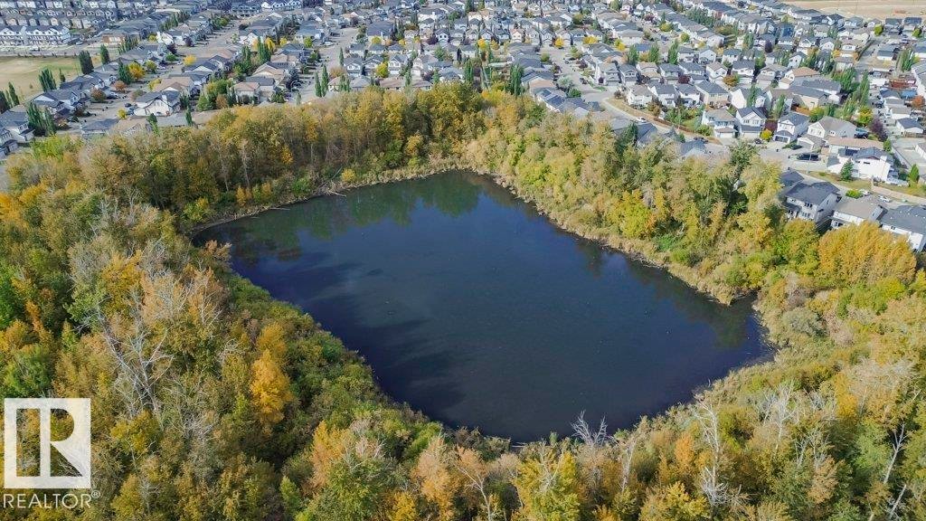 Aerial view showcasing the surrounding neighborhood, featuring a body of water encircled by trees, and residential properties with varied roof colors - 320 Secord Boulevard, Edmonton, AB - Outdoor With Body Of Water With View
