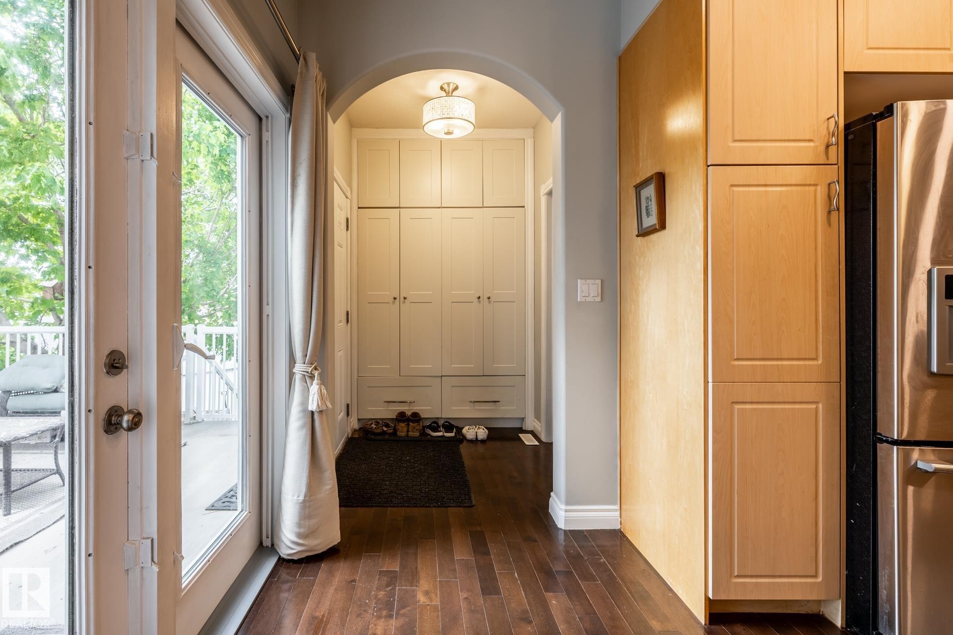 Hardwood flooring extends throughout this space featuring a built-in storage unit with archway, a glass-paneled door opening to an exterior deck with white railing, and wood-finish cabinetry - 2036 Towne Centre Boulevard, Edmonton, AB - Indoor Photo Showing Other Room