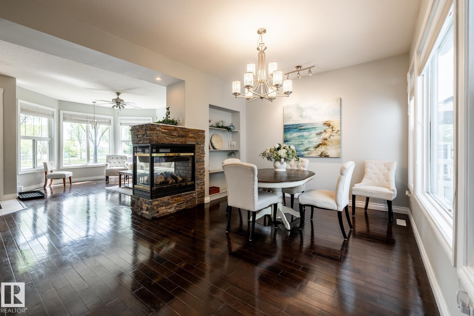 Spacious interior featuring dark wood-finish flooring, a two-sided stone-clad fireplace, and an arched entryway - 2036 Towne Centre Boulevard, Edmonton, AB - Indoor Photo Showing Dining Room With Fireplace