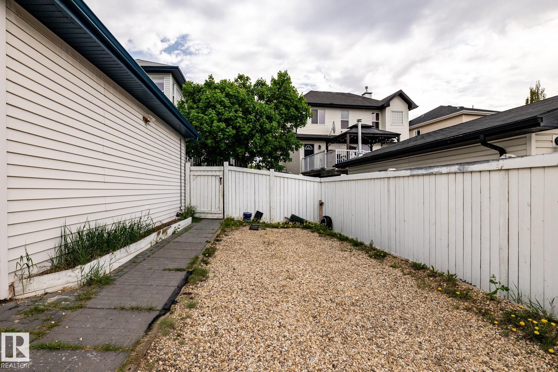 Gravel patio area featuring a white privacy fence and a paved pathway alongside the structure - 2036 Towne Centre Boulevard, Edmonton, AB - Outdoor