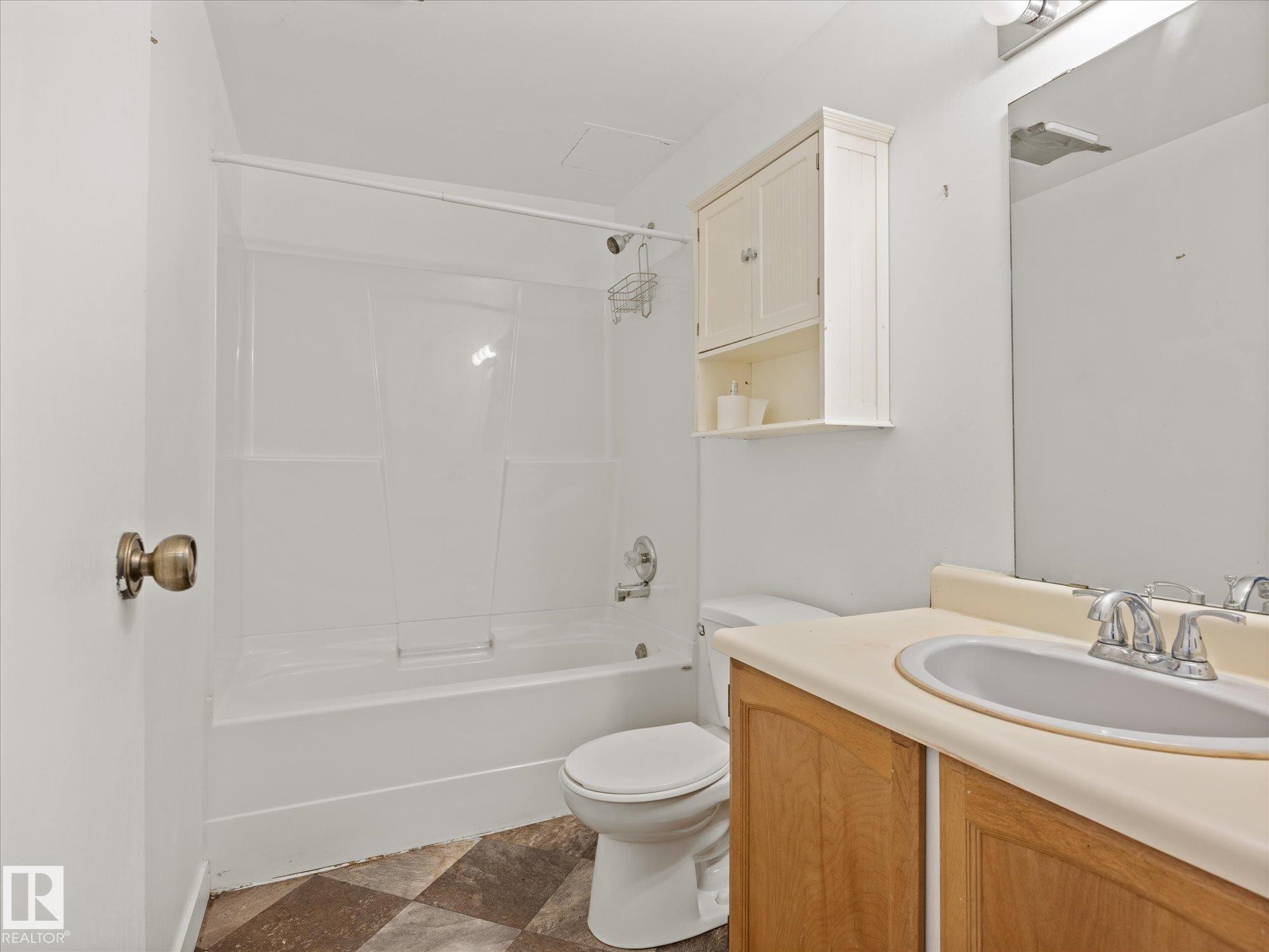 Bathroom featuring a full tub and shower combination with white surround, a single vanity with wood-finish cabinetry, a built-in mirror, and checkered flooring - 110 10139 117 Street, Edmonton, AB