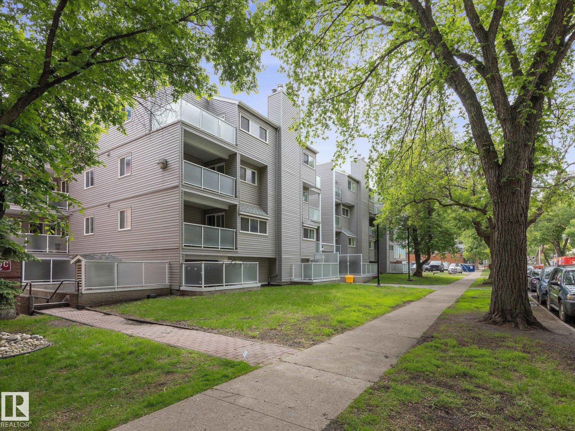 Multi-story residential building featuring gray horizontal siding and individual balconies with frosted glass railings - 110 10139 117 Street, Edmonton, AB
