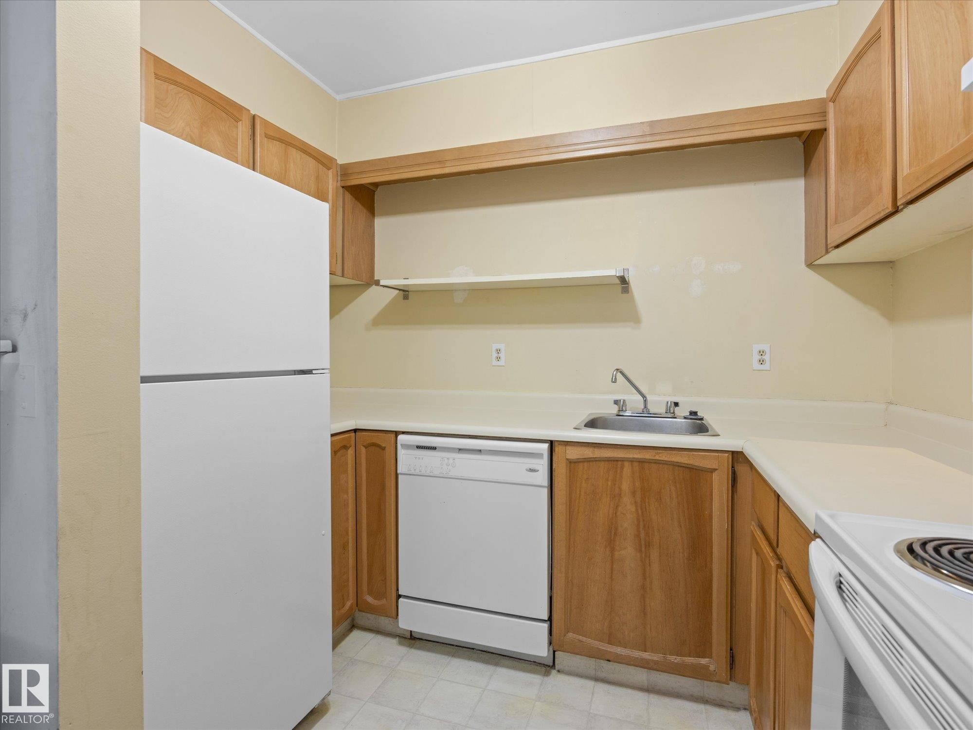 Compact kitchen featuring wood cabinetry, laminate countertops, a white refrigerator, a white dishwasher, and a white electric range - 110 10139 117 Street, Edmonton, AB