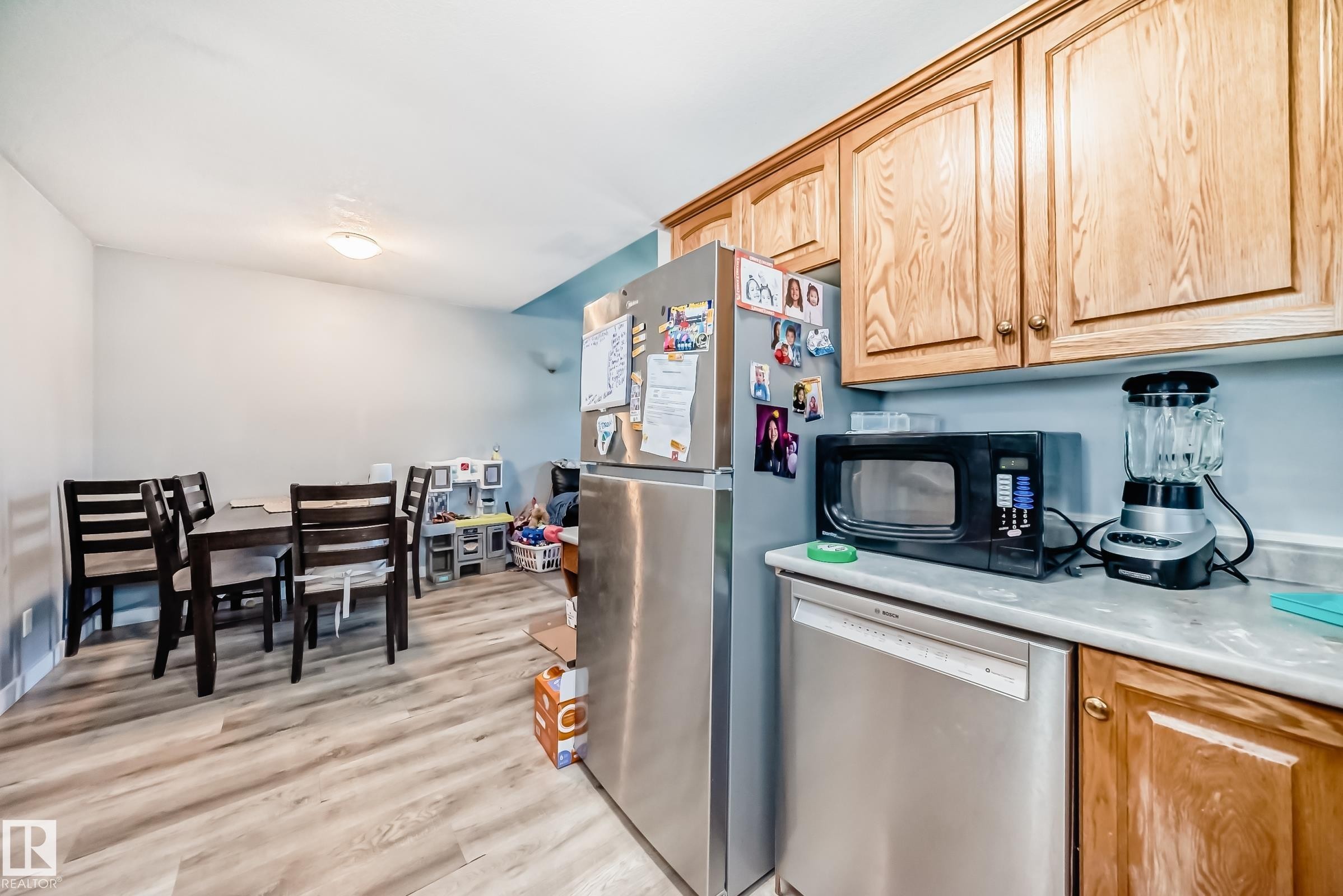 Open-concept kitchen and dining area featuring wood-finish flooring, light wood cabinetry, and a stainless steel dishwasher - 10017 153 Street, Edmonton, AB - Indoor