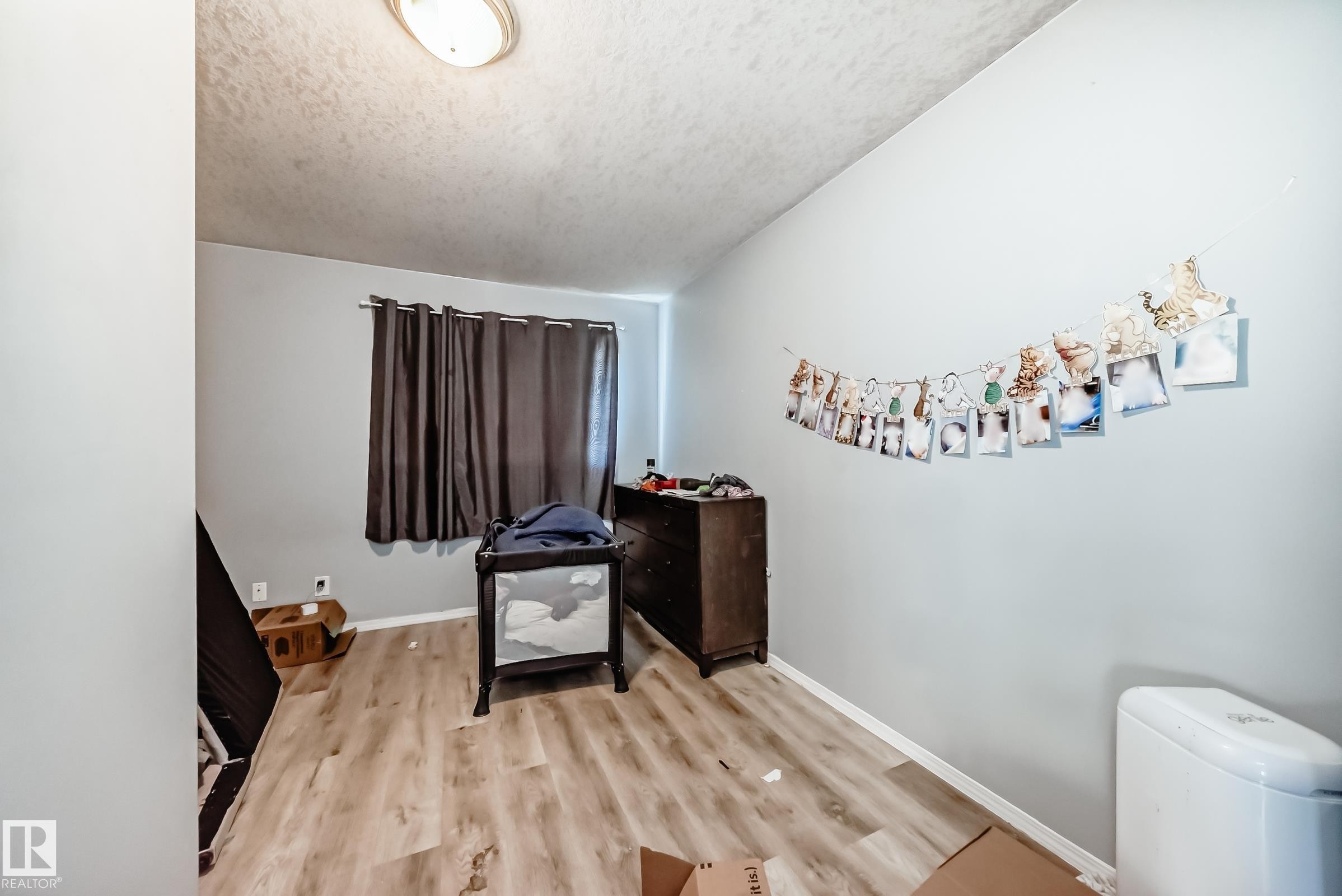 Room featuring light wood-finish flooring, light gray walls, and a window with dark curtains - 10017 153 Street, Edmonton, AB - Indoor