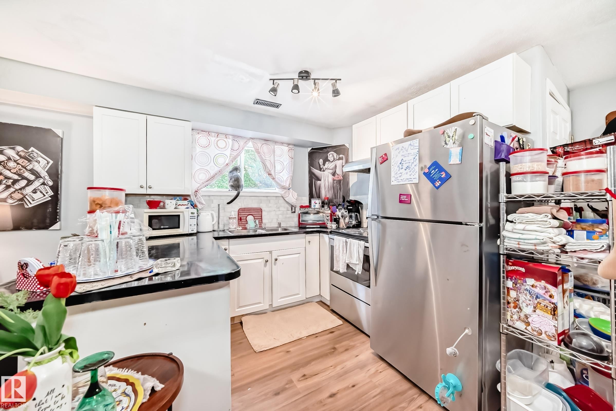 Kitchen featuring wood-finish flooring, white cabinetry, dark countertops, a tile backsplash, and a stainless steel refrigerator - 10017 153 Street, Edmonton, AB - Indoor Photo Showing Kitchen