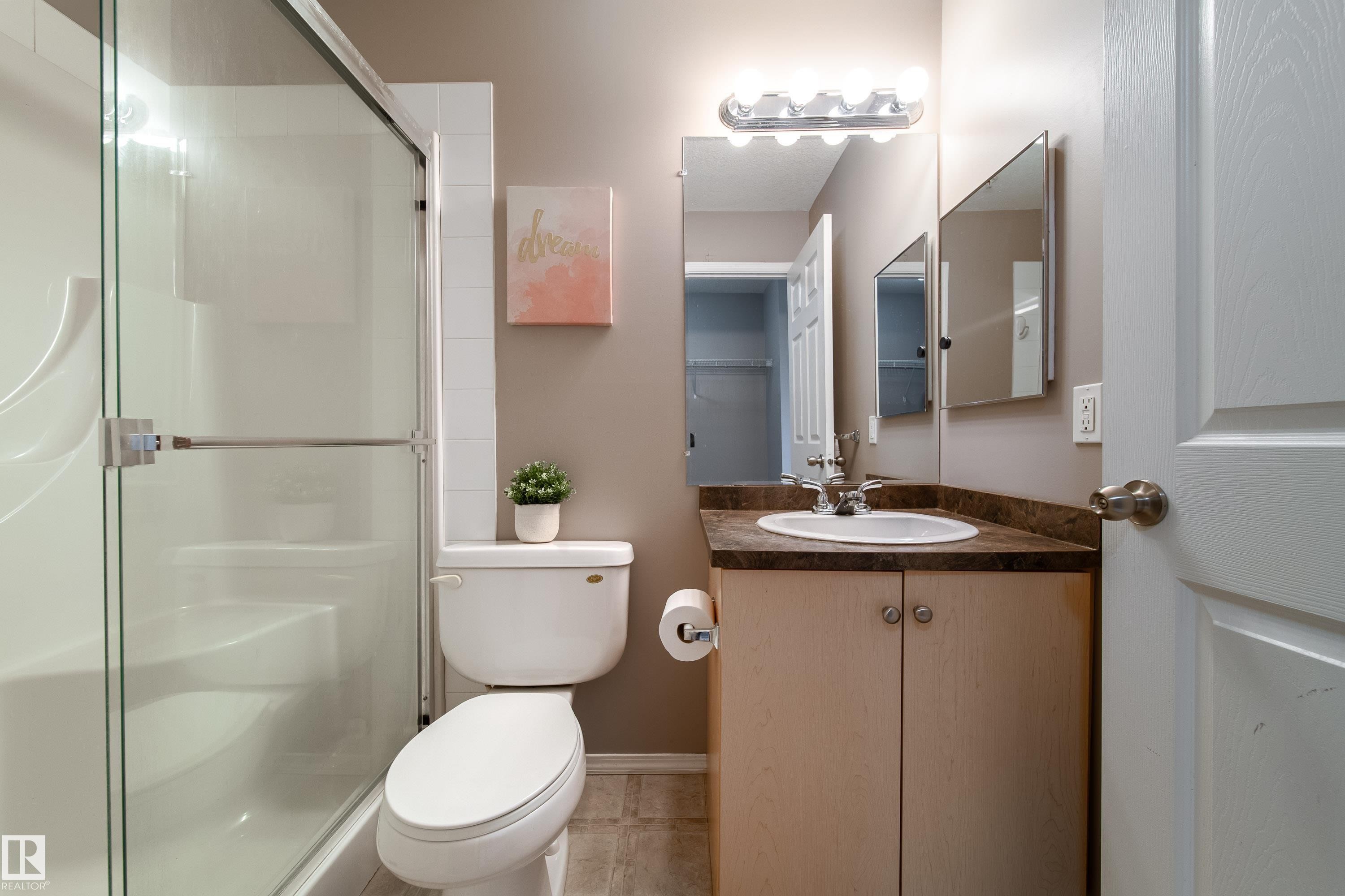 Bathroom featuring a white toilet, enclosed shower with glass doors, single vanity with a laminate countertop, and wood-finish flooring - 115 4309 33 Street, Stony Plain, AB