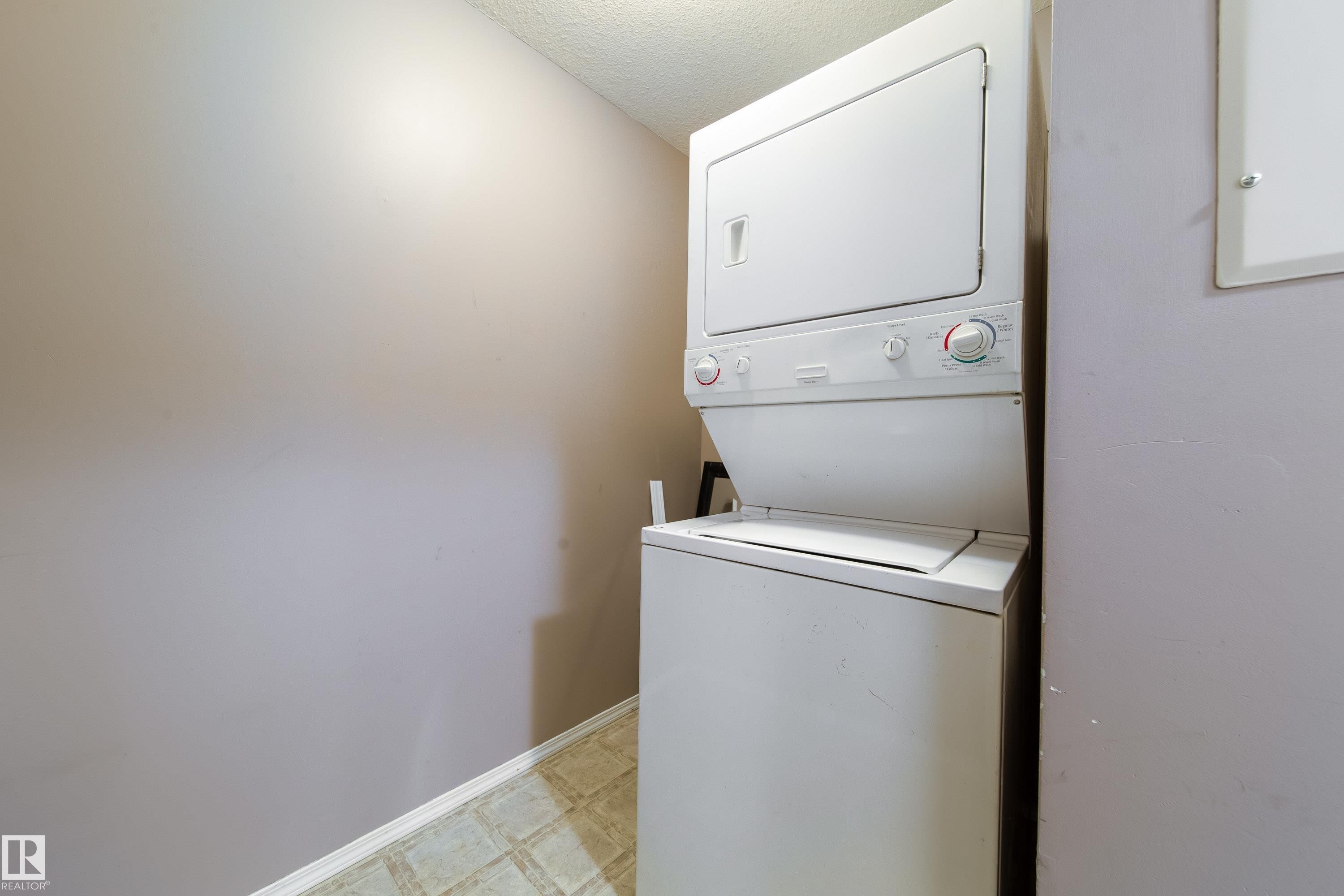 Dedicated laundry space featuring a stacked white washer and dryer unit, neutral wall color, and patterned floor tiling - 115 4309 33 Street, Stony Plain, AB