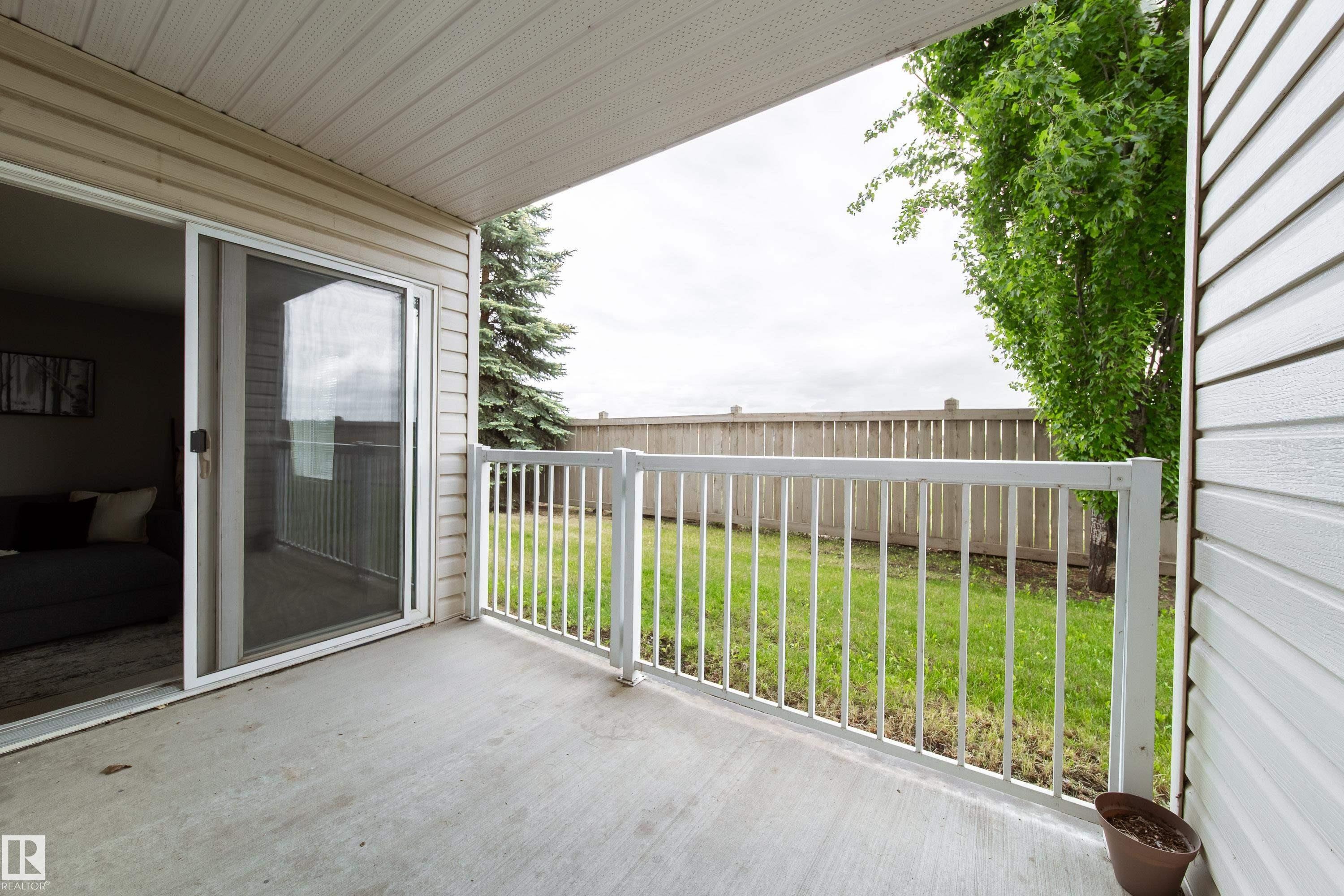 Covered concrete patio featuring white railing, direct access to the interior via a sliding glass door, and an exterior of horizontal siding - 115 4309 33 Street, Stony Plain, AB