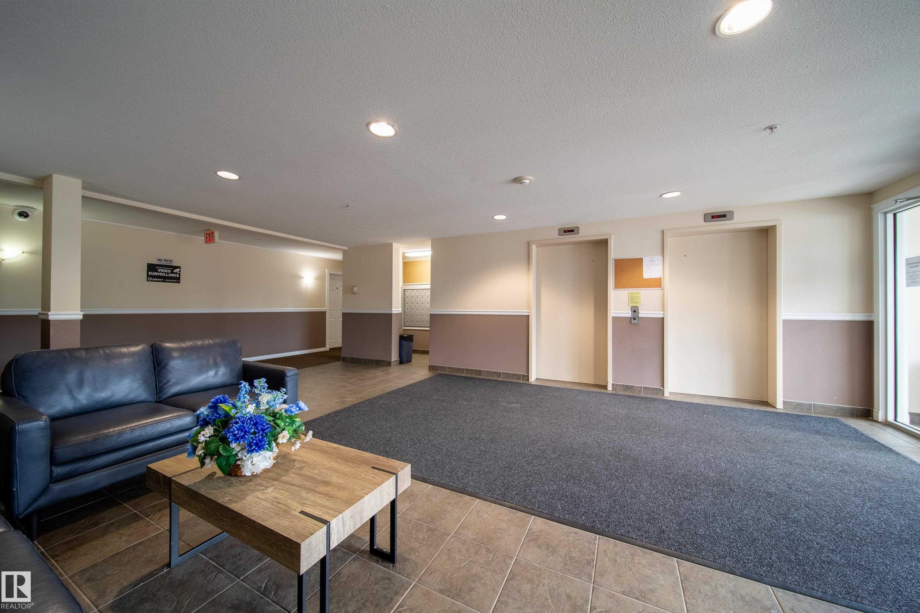 Spacious hallway featuring recessed lighting, two elevators, and a glass-paneled entry door - 115 4309 33 Street, Stony Plain, AB