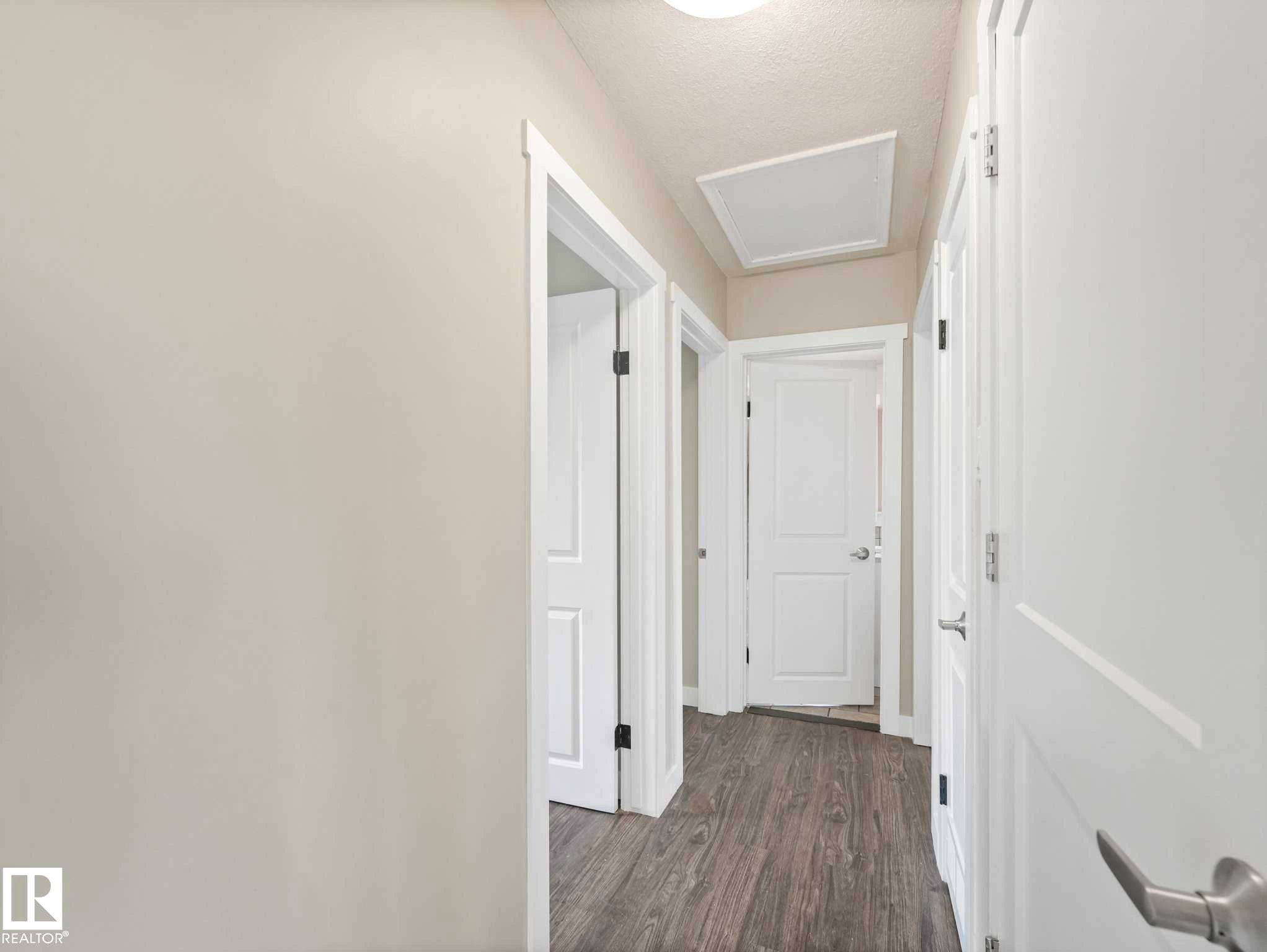 Hallway featuring wood-finish flooring, light-toned walls, multiple paneled doors, and a ceiling-mounted light fixture - 12241 54 Street Nw, Edmonton, AB - Indoor Photo Showing Other Room