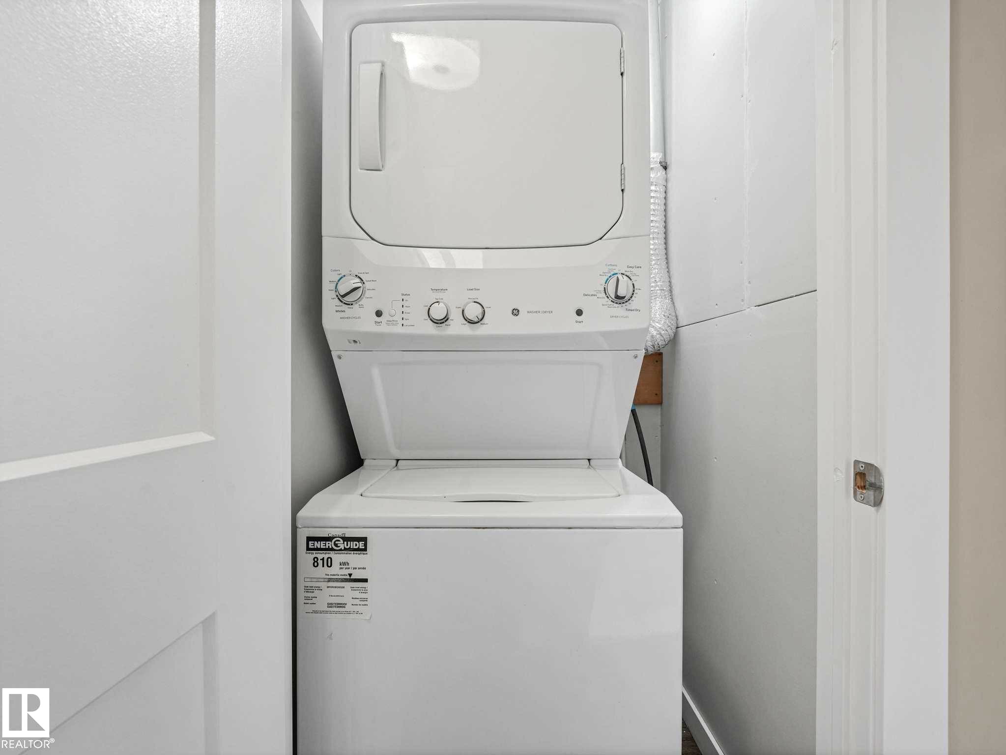 Dedicated laundry closet featuring a white stacked washer and dryer unit, white walls, and a light-colored door with a brushed nickel handle - 12241 54 Street Nw, Edmonton, AB - Indoor Photo Showing Laundry Room