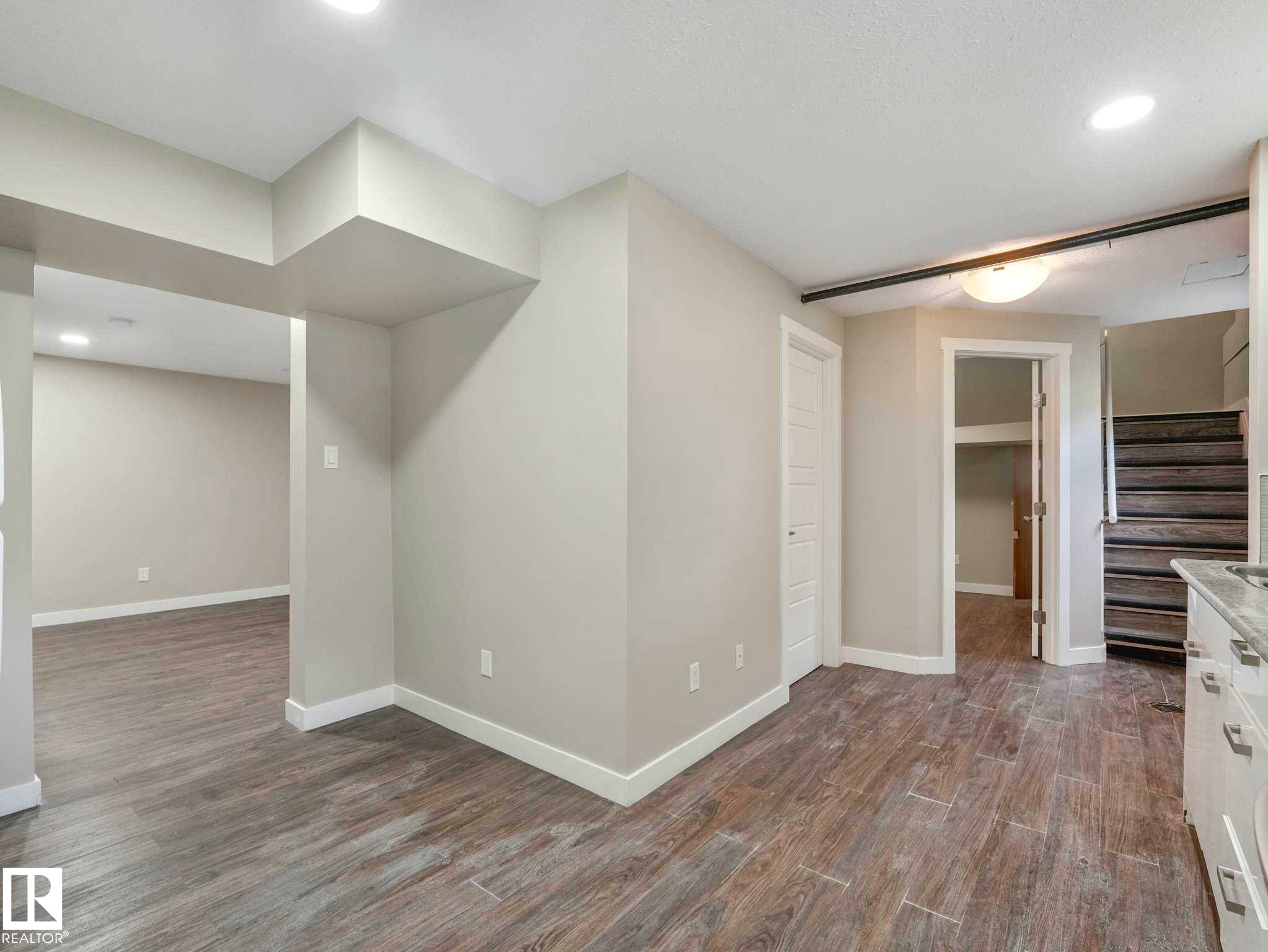 Spacious interior featuring wood-finish flooring, light neutral wall tones, recessed lighting, and white trim - 12241 54 Street Nw, Edmonton, AB - Indoor Photo Showing Other Room