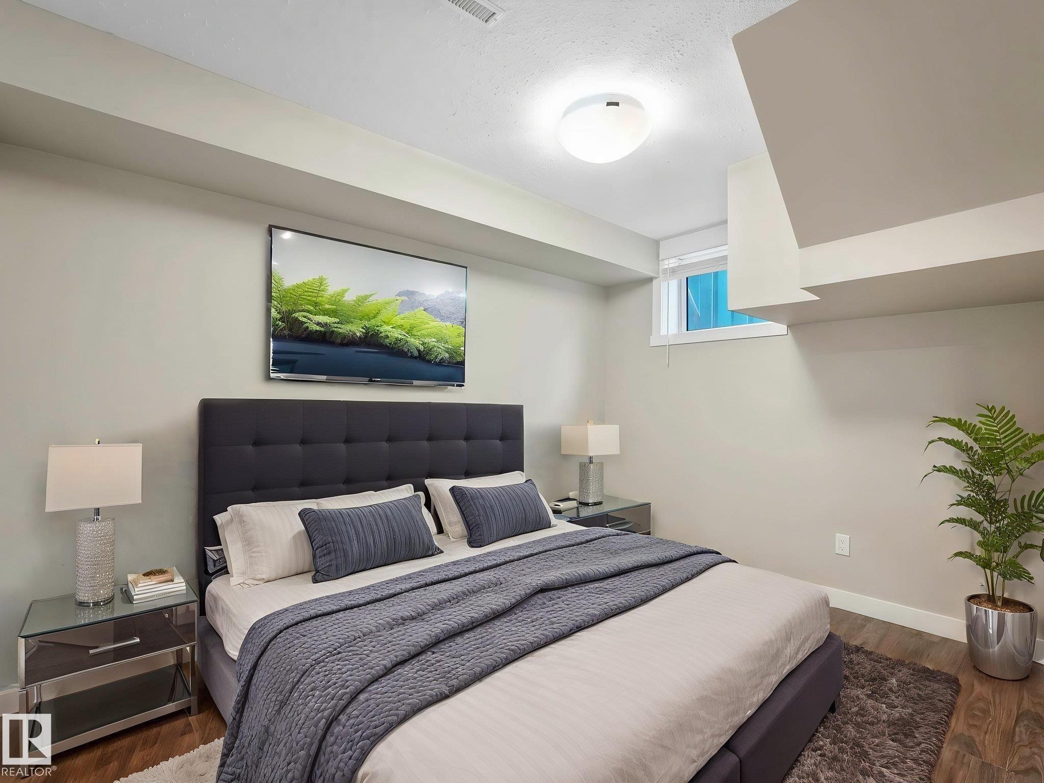 Bedroom featuring wood-finish flooring, a wall-mounted television, and a window with white trim - 12241 54 Street Nw, Edmonton, AB - Indoor Photo Showing Bedroom