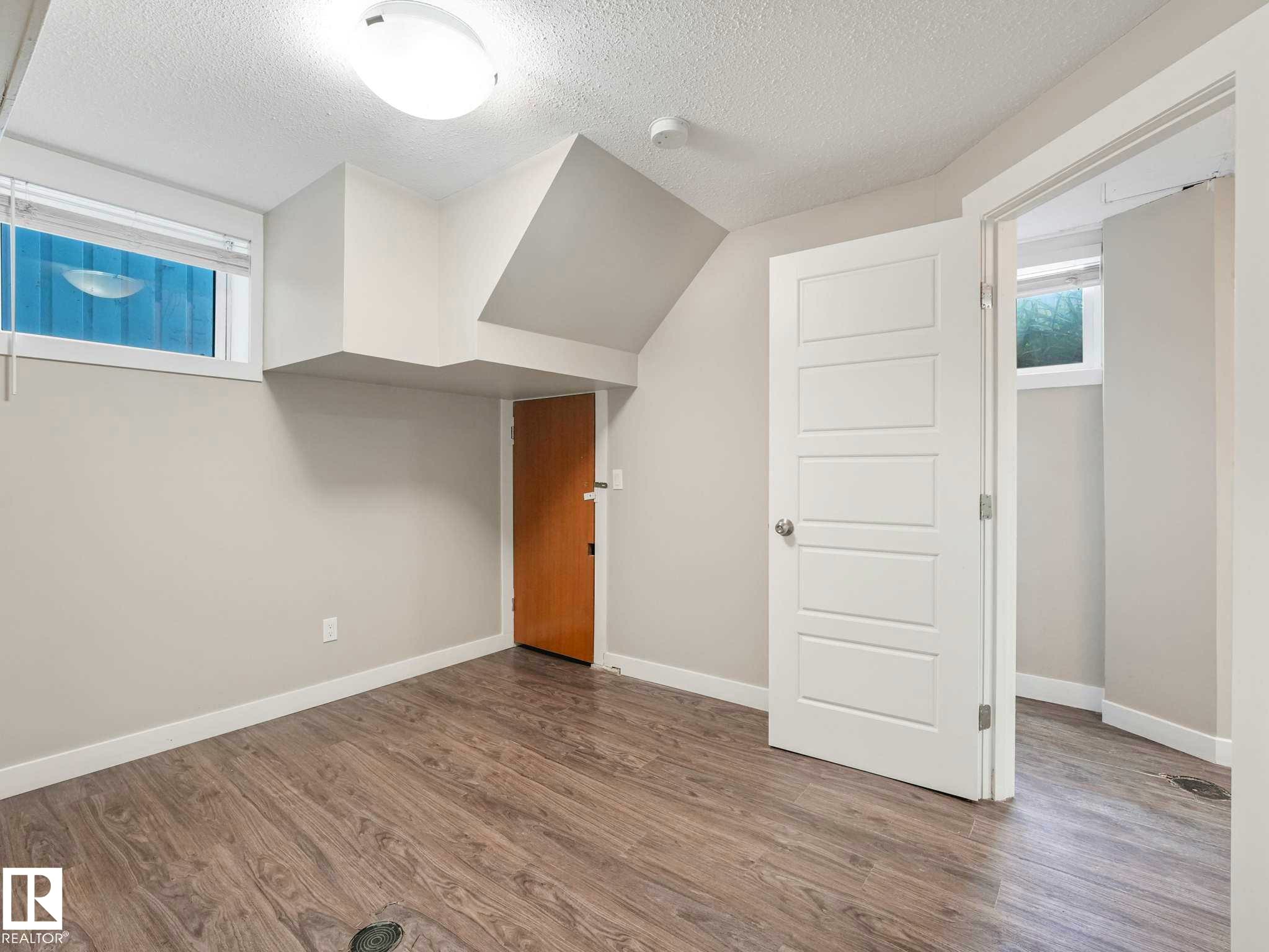 Room featuring wood-finish flooring, a contemporary overhead light fixture, and light gray wall tones - 12241 54 Street Nw, Edmonton, AB - Indoor Photo Showing Other Room