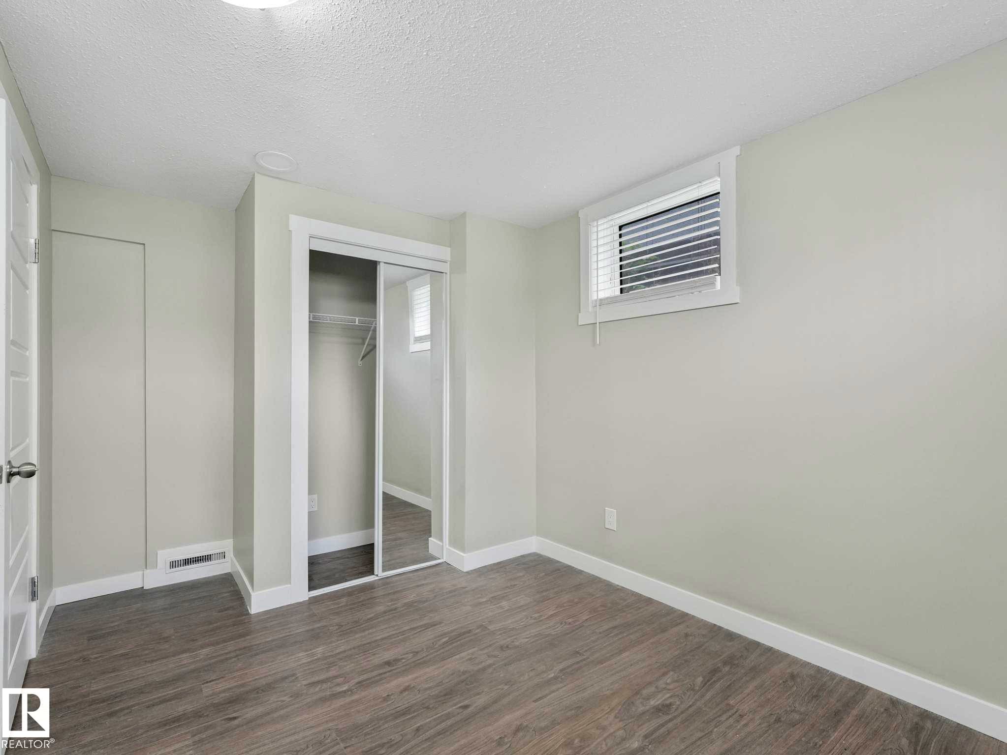 Bright room featuring light wood-finish flooring, a mirrored closet with sliding doors, white trim, and a window with blinds - 12241 54 Street Nw, Edmonton, AB - Indoor Photo Showing Other Room