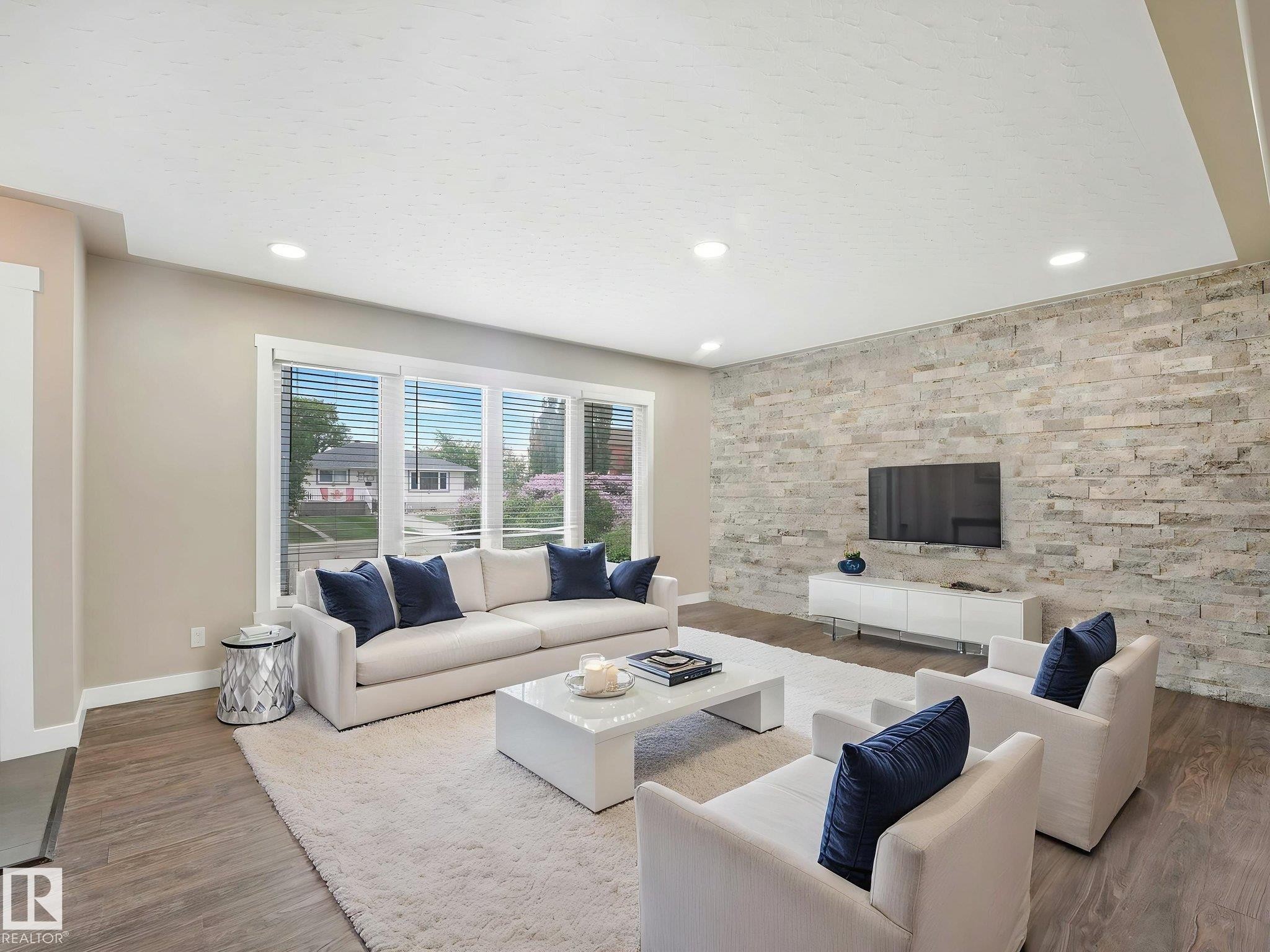 Spacious living area featuring a stacked stone accent wall, wood-finish flooring, and recessed ceiling lighting - 12241 54 Street Nw, Edmonton, AB - Indoor Photo Showing Living Room