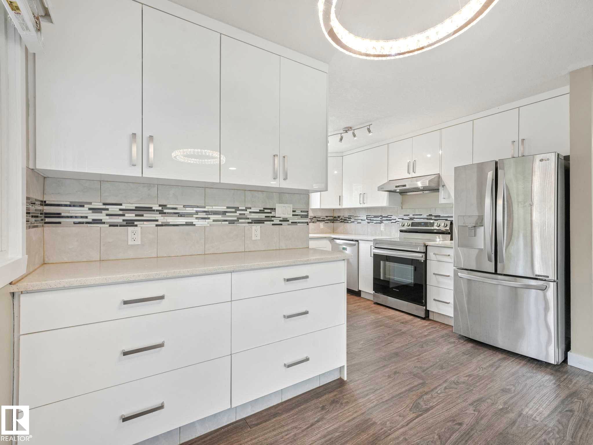 Kitchen featuring white cabinetry, stone-finish countertops, stainless steel appliances, a decorative backsplash with accent tiles, and wood-finish flooring - 12241 54 Street Nw, Edmonton, AB - Indoor Photo Showing Kitchen With Upgraded Kitchen