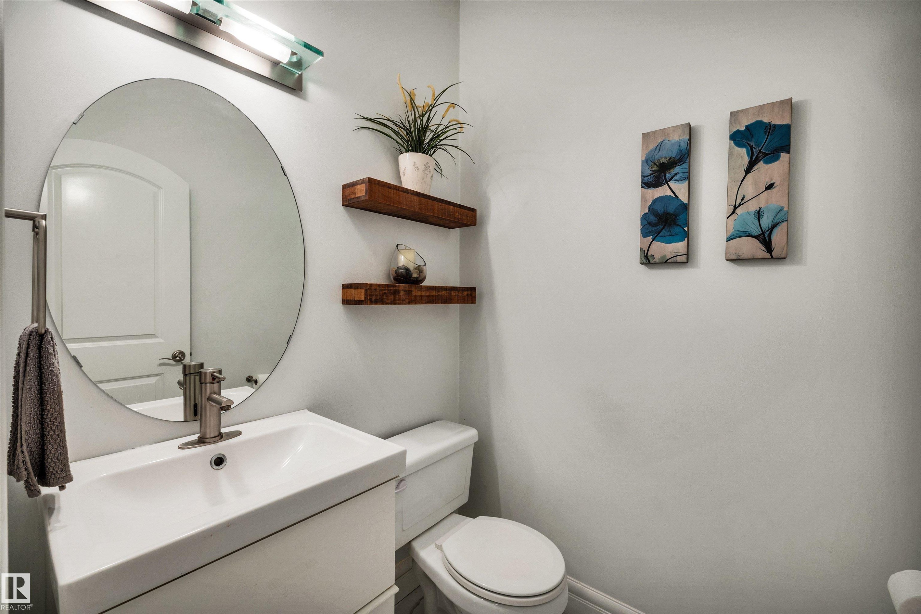 Bathroom featuring a white vanity with integrated sink, brushed nickel faucet, and a large circular mirror - 11935 21 Avenue, Edmonton, AB