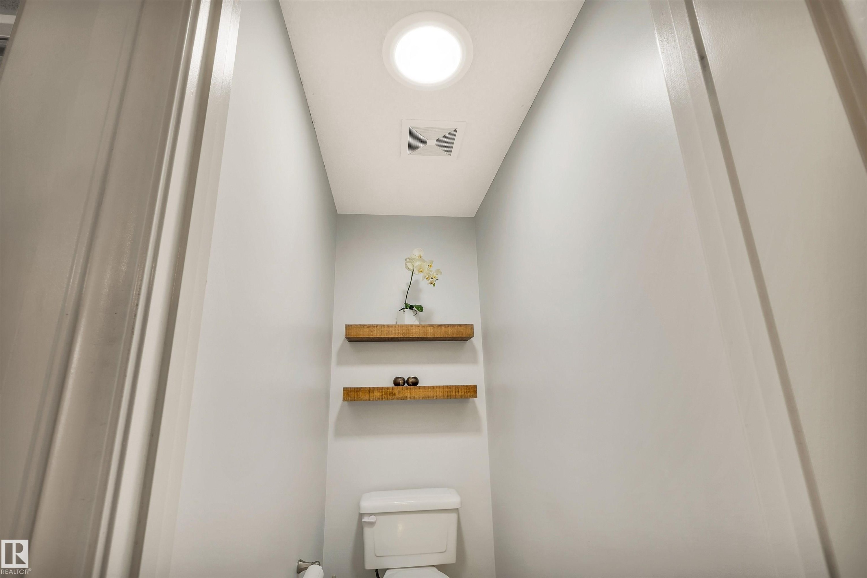 Bright interior space featuring a circular ceiling light fixture, a white toilet, and two floating wood shelves - 11935 21 Avenue, Edmonton, AB