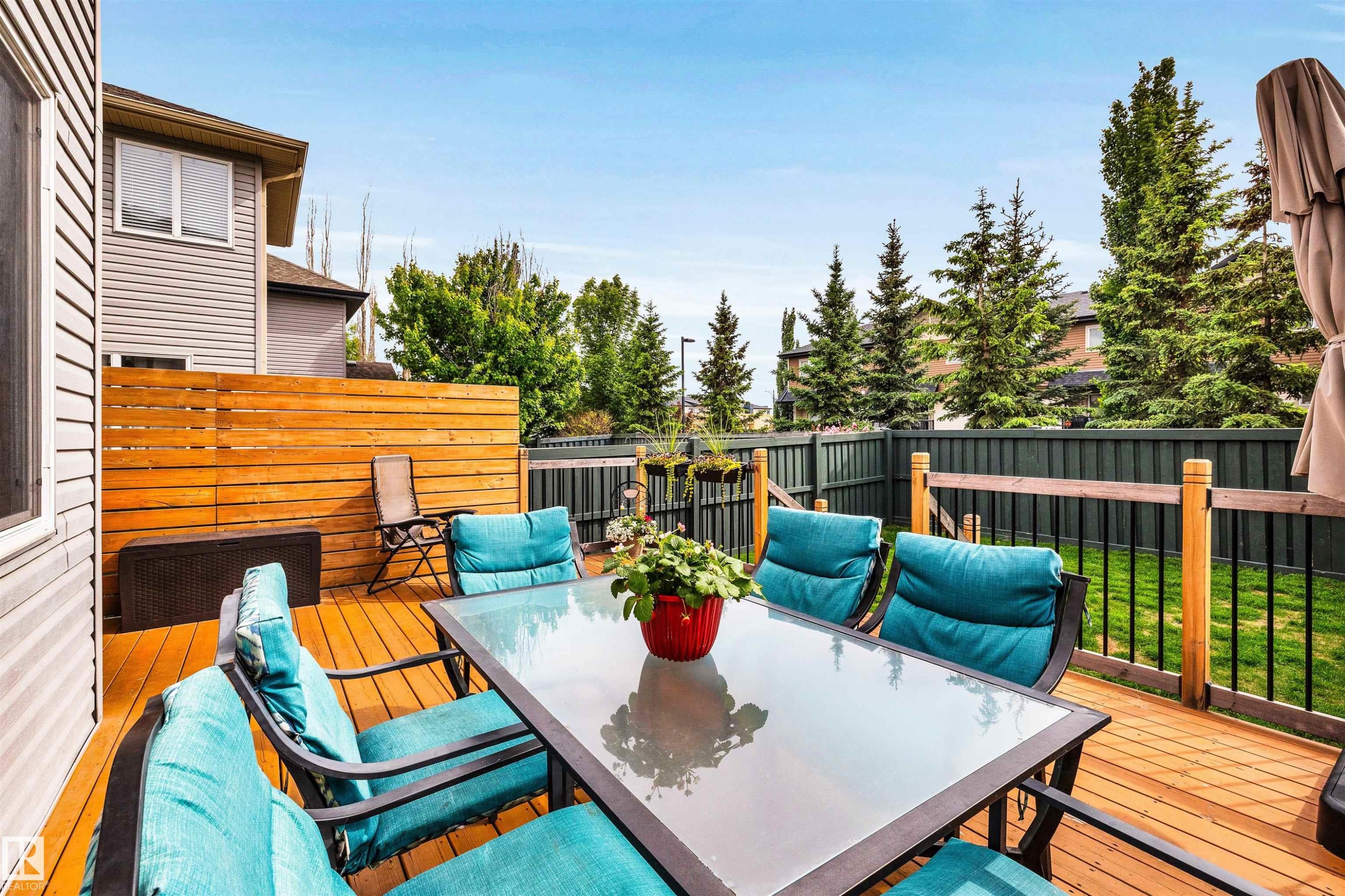 Spacious wood deck featuring a clear glass-top outdoor dining table, a slatted privacy screen, and durable vinyl siding on the adjacent structure - 11935 21 Avenue, Edmonton, AB