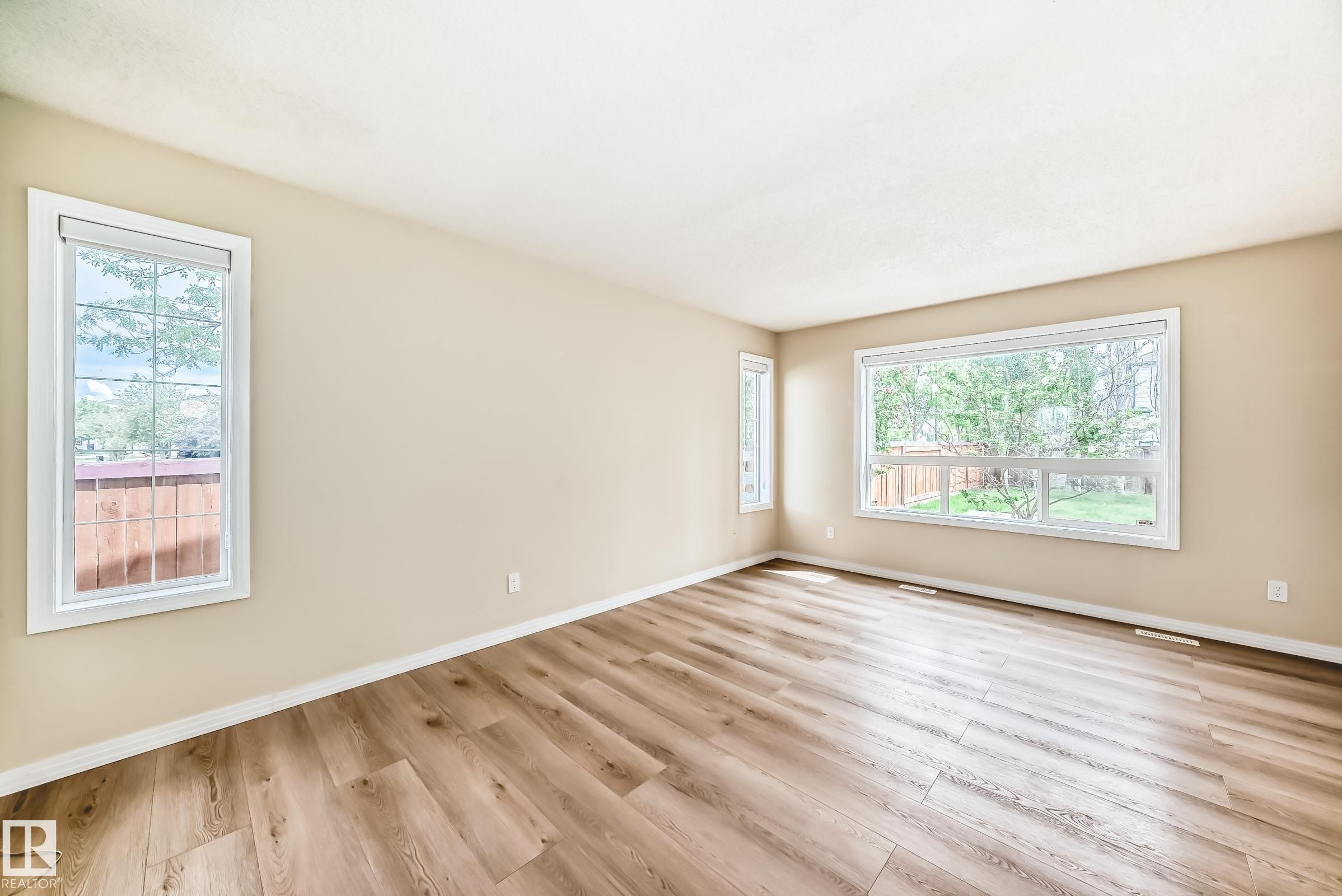 Spacious room featuring wood-finish flooring, light-toned walls, multiple large windows with white trim, and white baseboards - 3711 22A St, Edmonton, AB