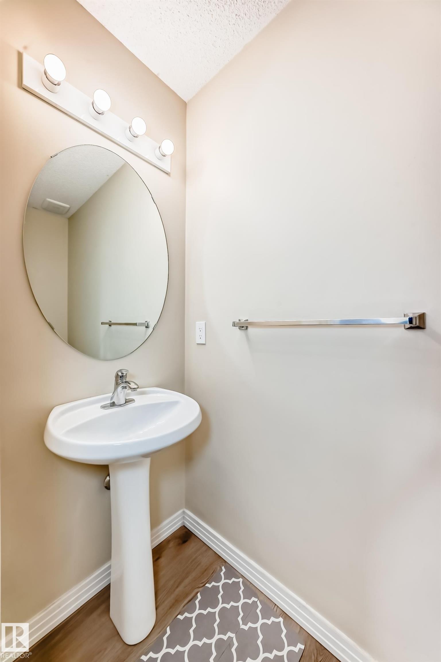 Pedestal sink with chrome faucet, complemented by a circular mirror and a four-bulb vanity light fixture - 3711 22A St, Edmonton, AB