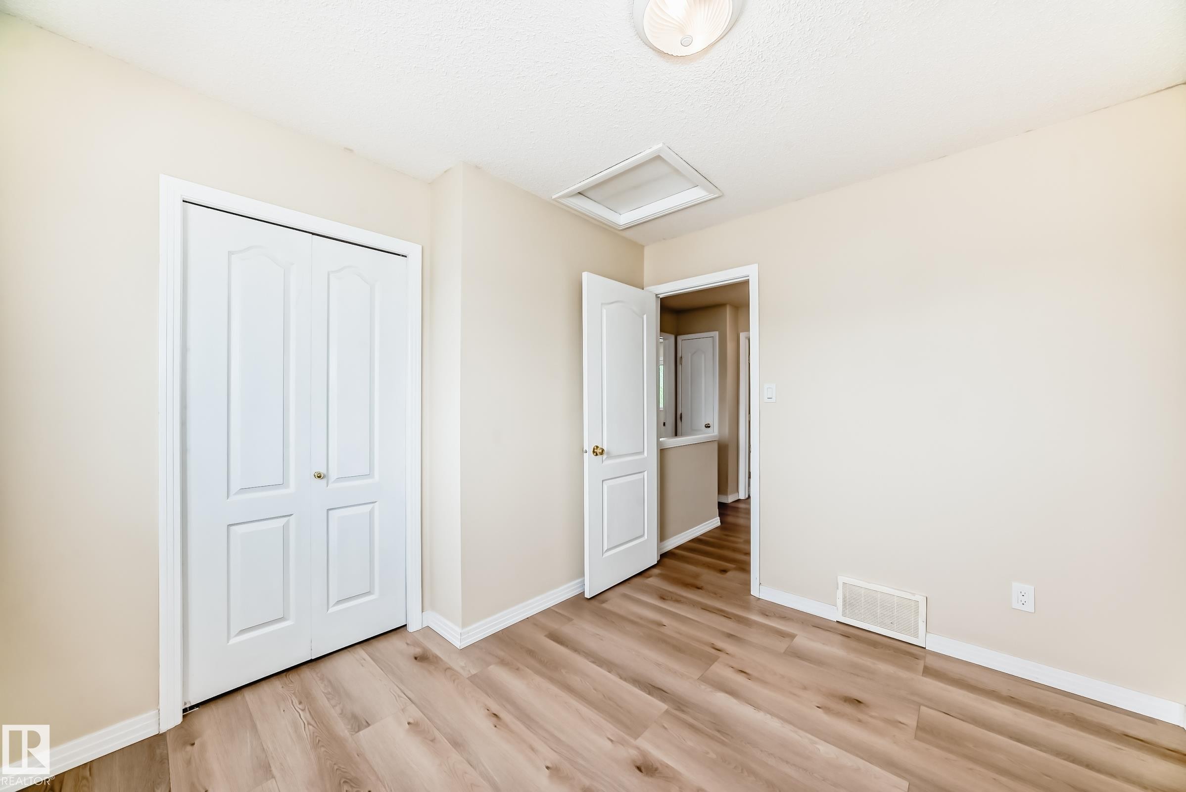 Room with wood-finish flooring, light-toned walls, white baseboards, and a bi-fold closet door - 3711 22A St, Edmonton, AB