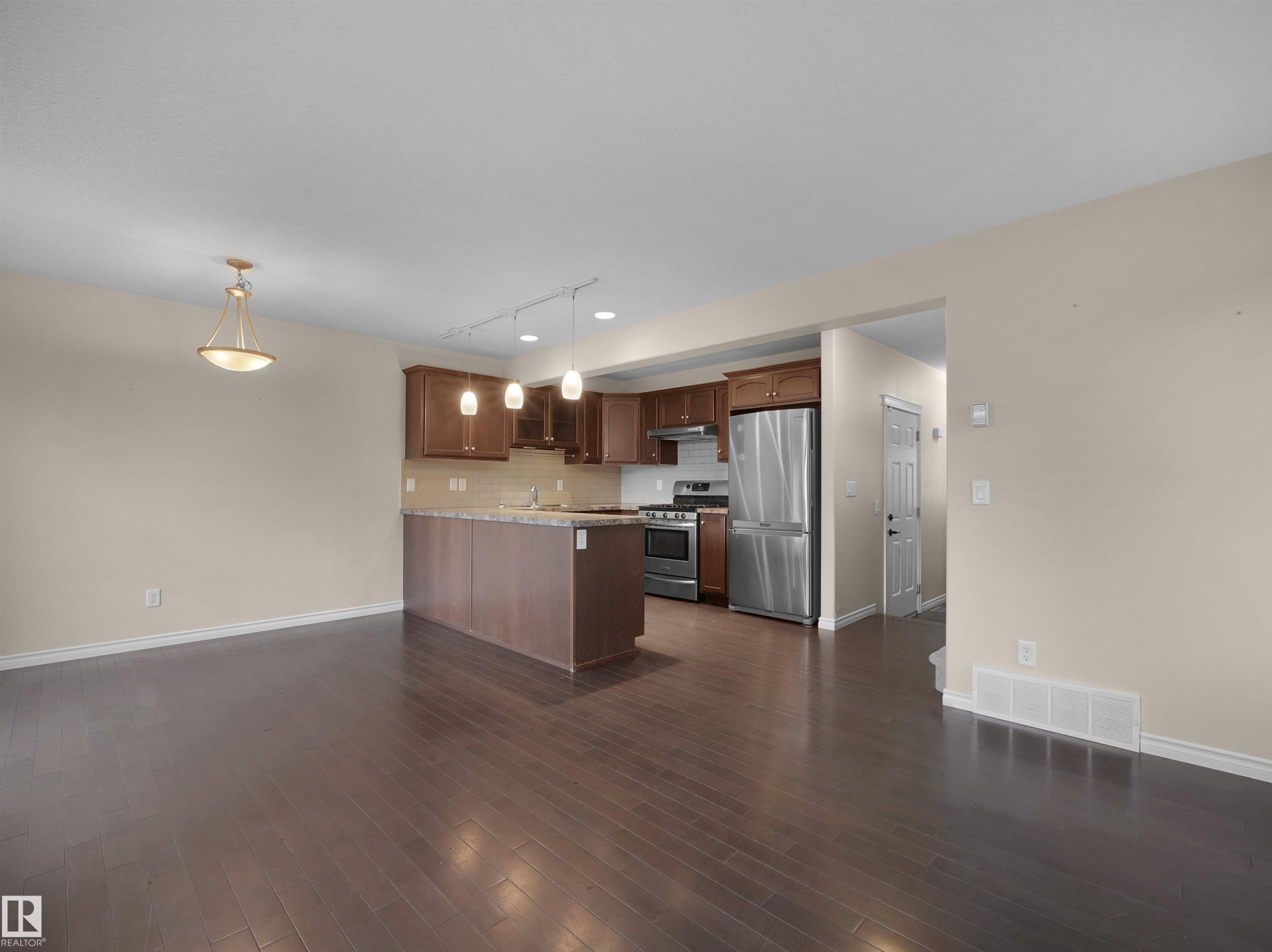 Open-concept living space featuring wood-finish flooring, a kitchen island with seating, stainless steel appliances, dark wood cabinetry, and recessed lighting - 21316 45A Avenue Nw, Edmonton, AB