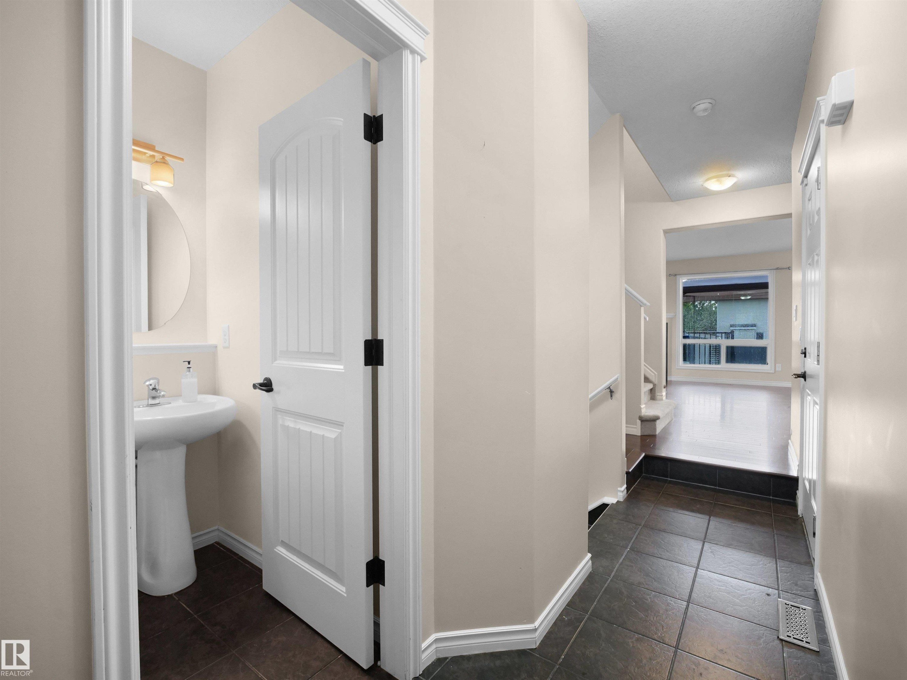 Entryway featuring dark tile flooring, leading to a space with wood-finish flooring and a large window - 21316 45A Avenue Nw, Edmonton, AB