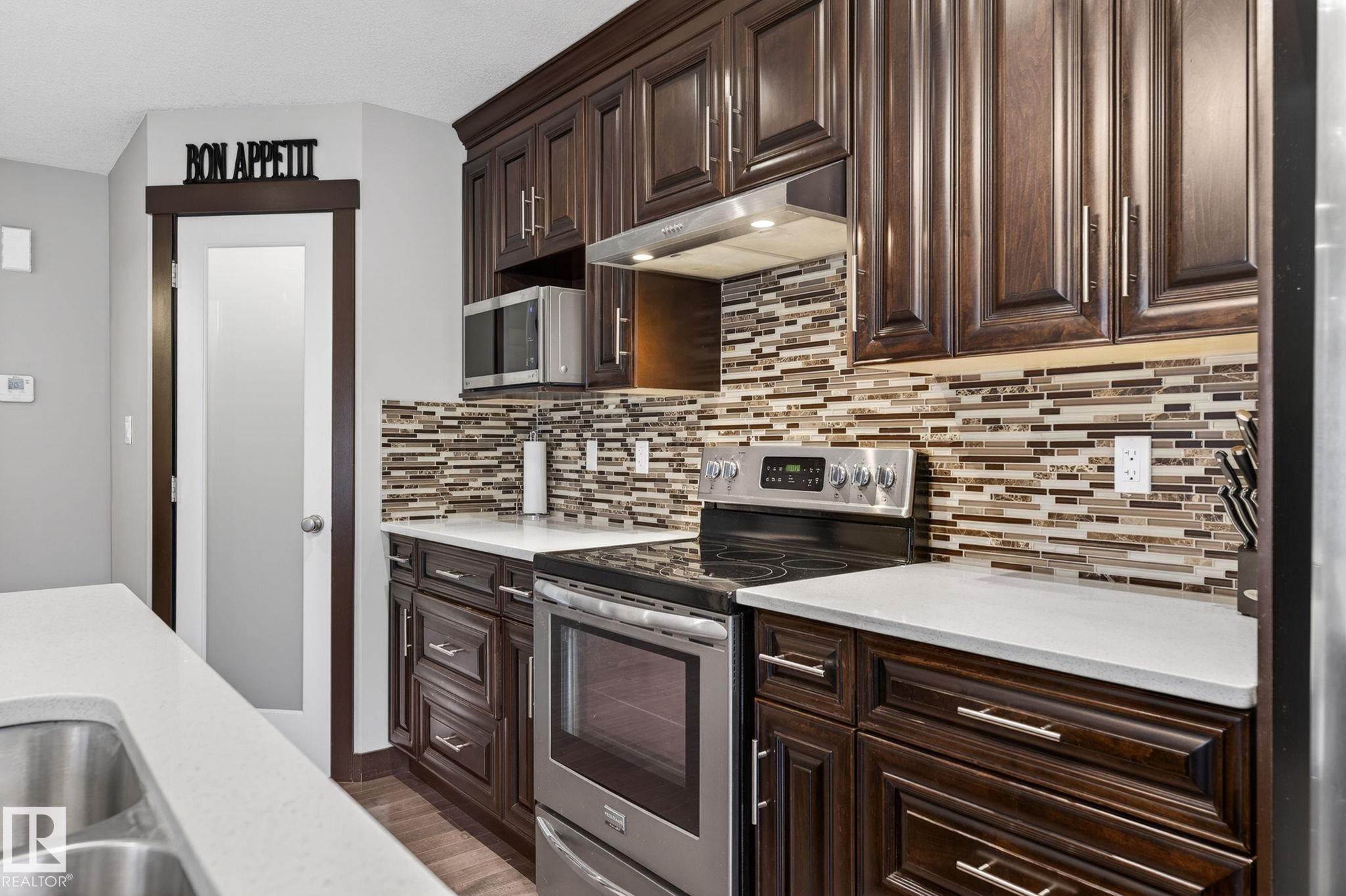 Kitchen featuring dark wood-finish cabinetry, light-toned countertops, and a full tile backsplash - 8506 80 Avenue, Edmonton, AB