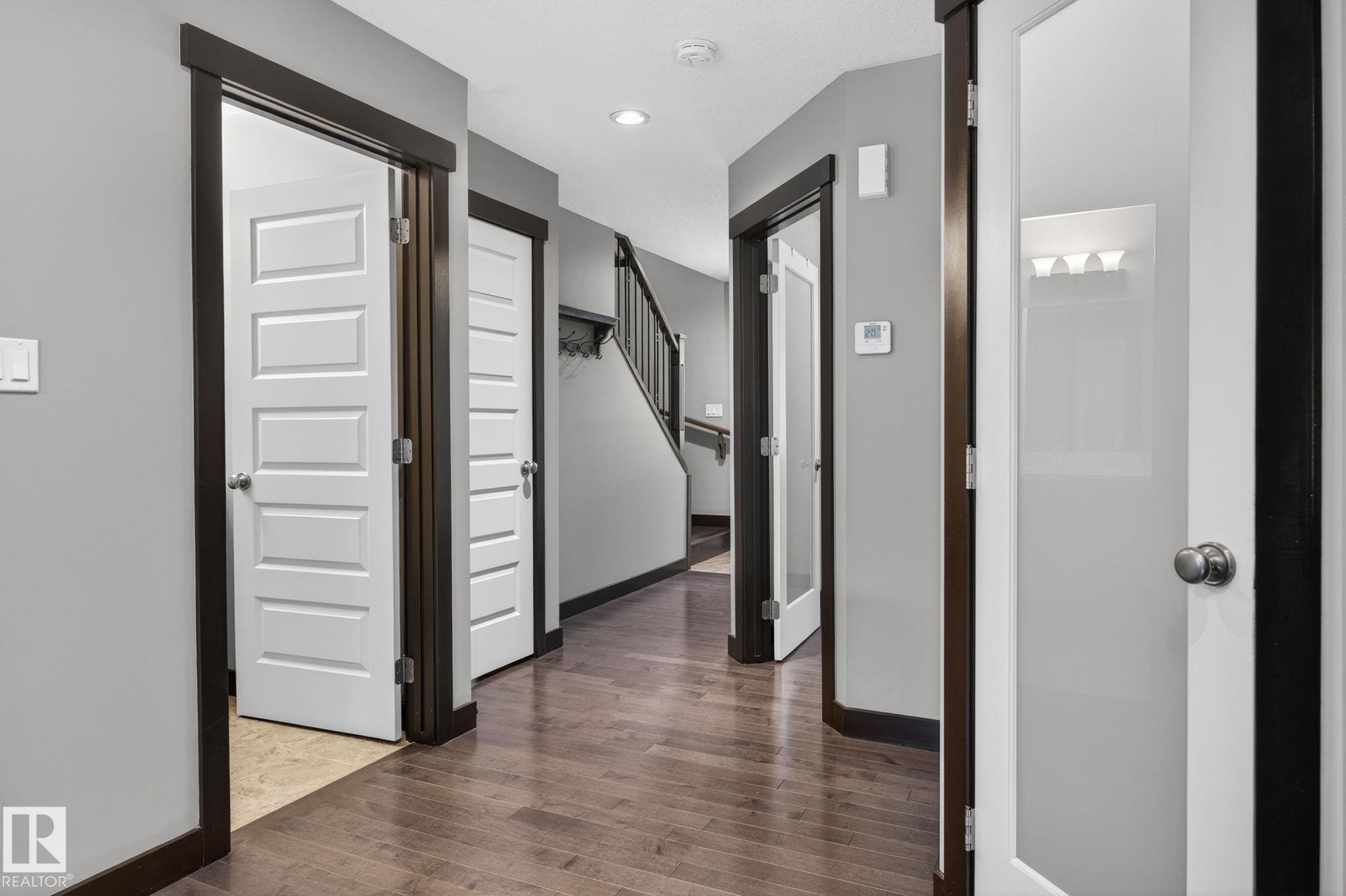 Hallway featuring wood-finish flooring, recessed lighting, white five-panel interior doors with dark wood trim, and a frosted glass panel door - 8506 80 Avenue, Edmonton, AB
